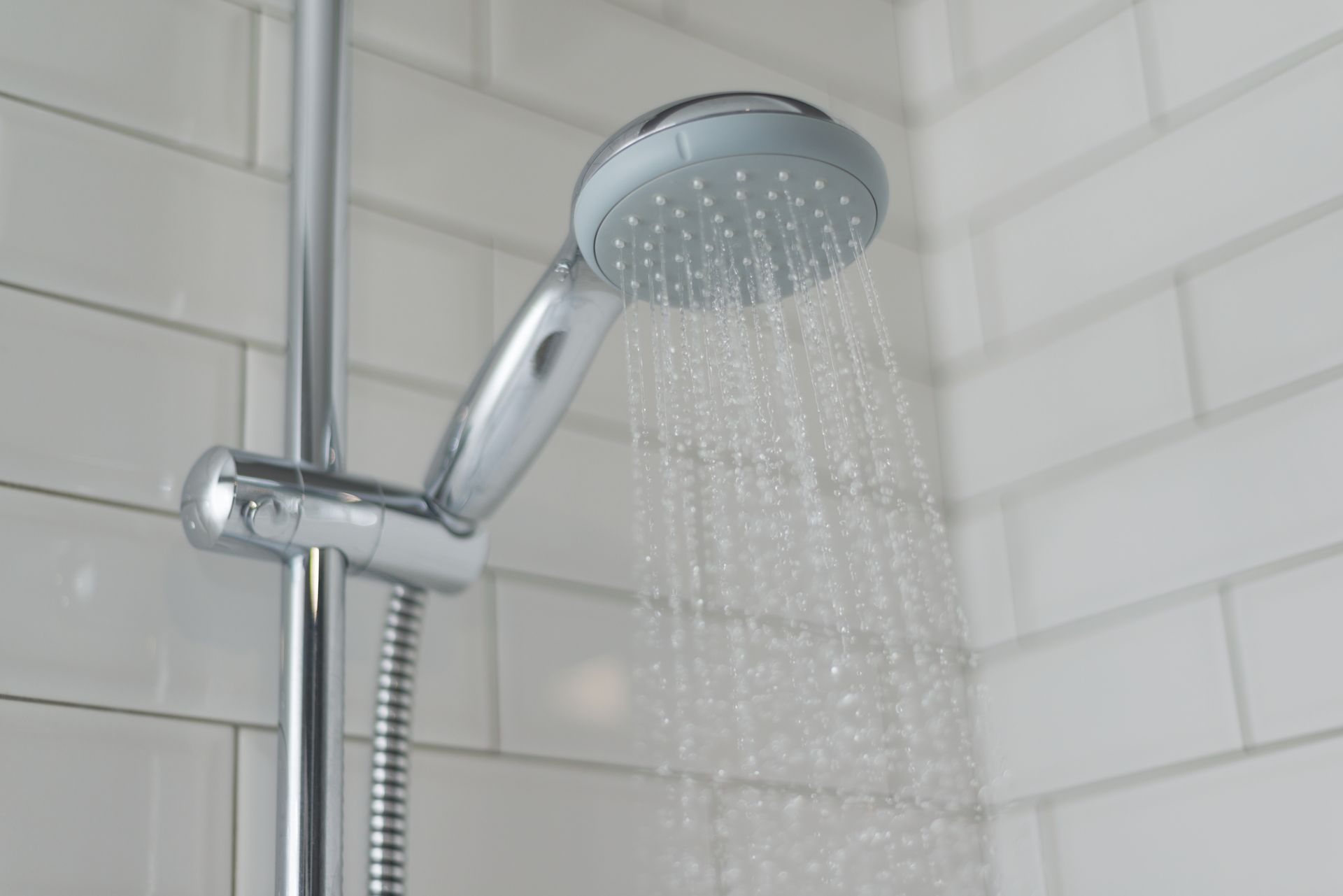 Chrome shower head spraying water in a tiled bathroom