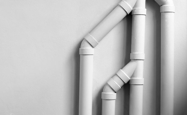 White PVC pipes with joints against a light gray wall White PVC pipes with joints against a light gray wall