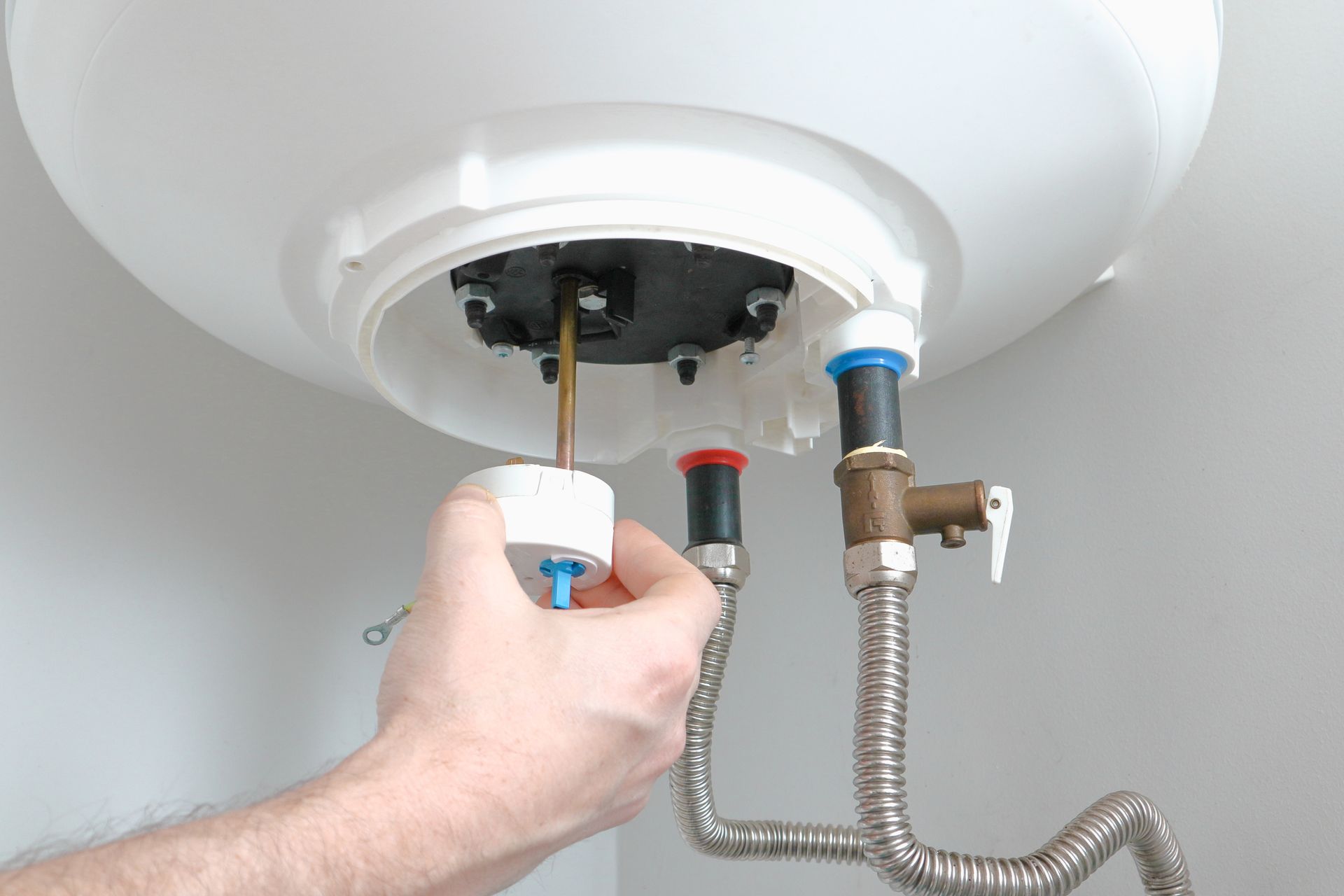 Hand connecting a water heater hose under a white tank in a utility space