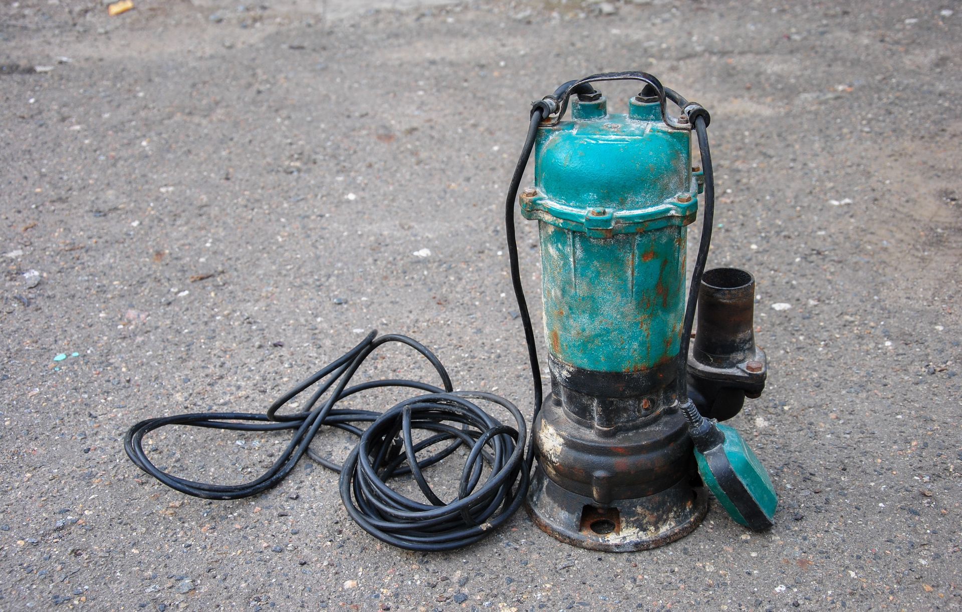 Teal submersible pump with black cord on concrete ground, shown with its side cover open.