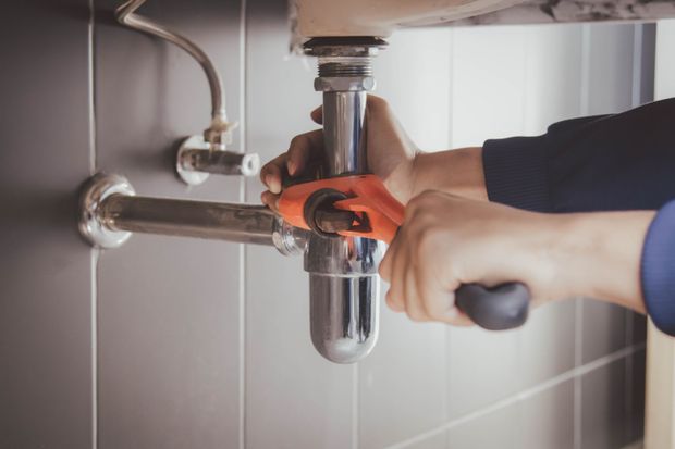 Hands using a red wrench to tighten a bathroom sink drain pipe under a sink