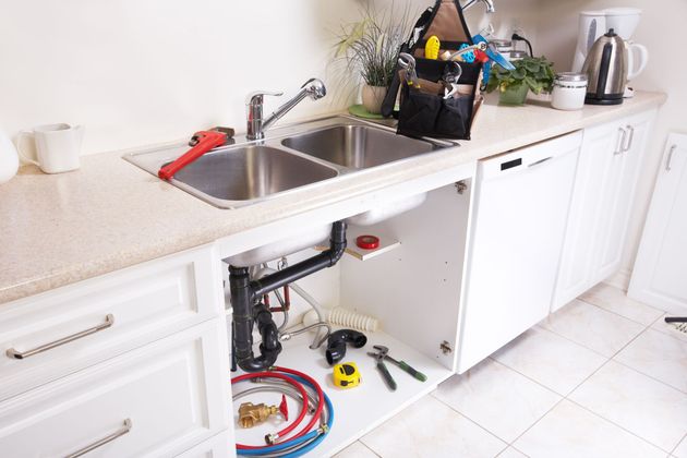 Bright kitchen countertop with sink, open cabinet exposing plumbing tools, and white cabinets on tiled floor Bright kitchen countertop with sink, open cabinet exposing plumbing tools, and white cabinets on tiled floor
