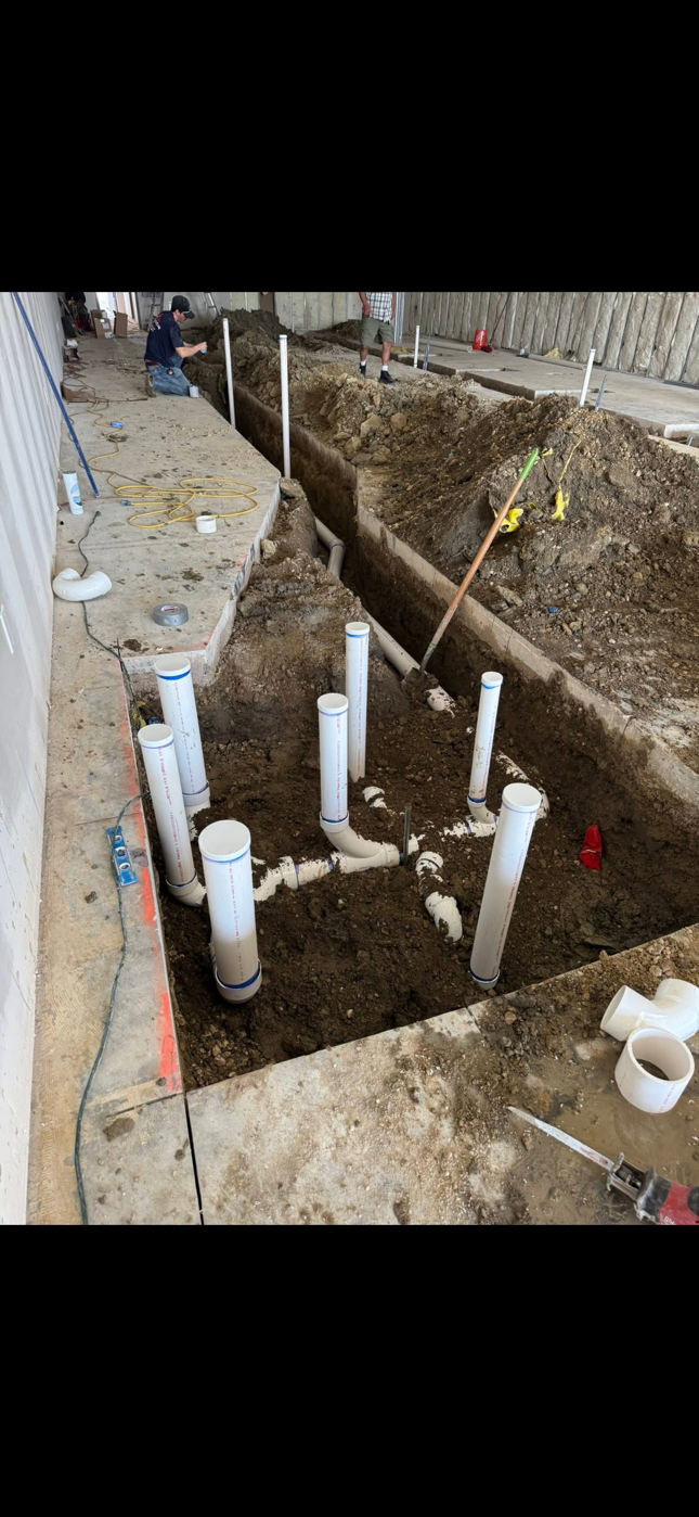 Construction trench with white PVC pipes and rough dirt excavation beside a building wall