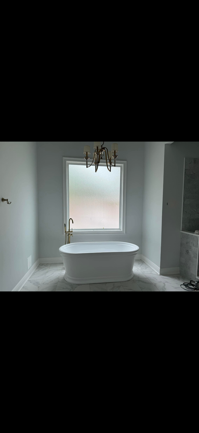 Freestanding white bathtub centered beneath a window in a bright, minimalist bathroom