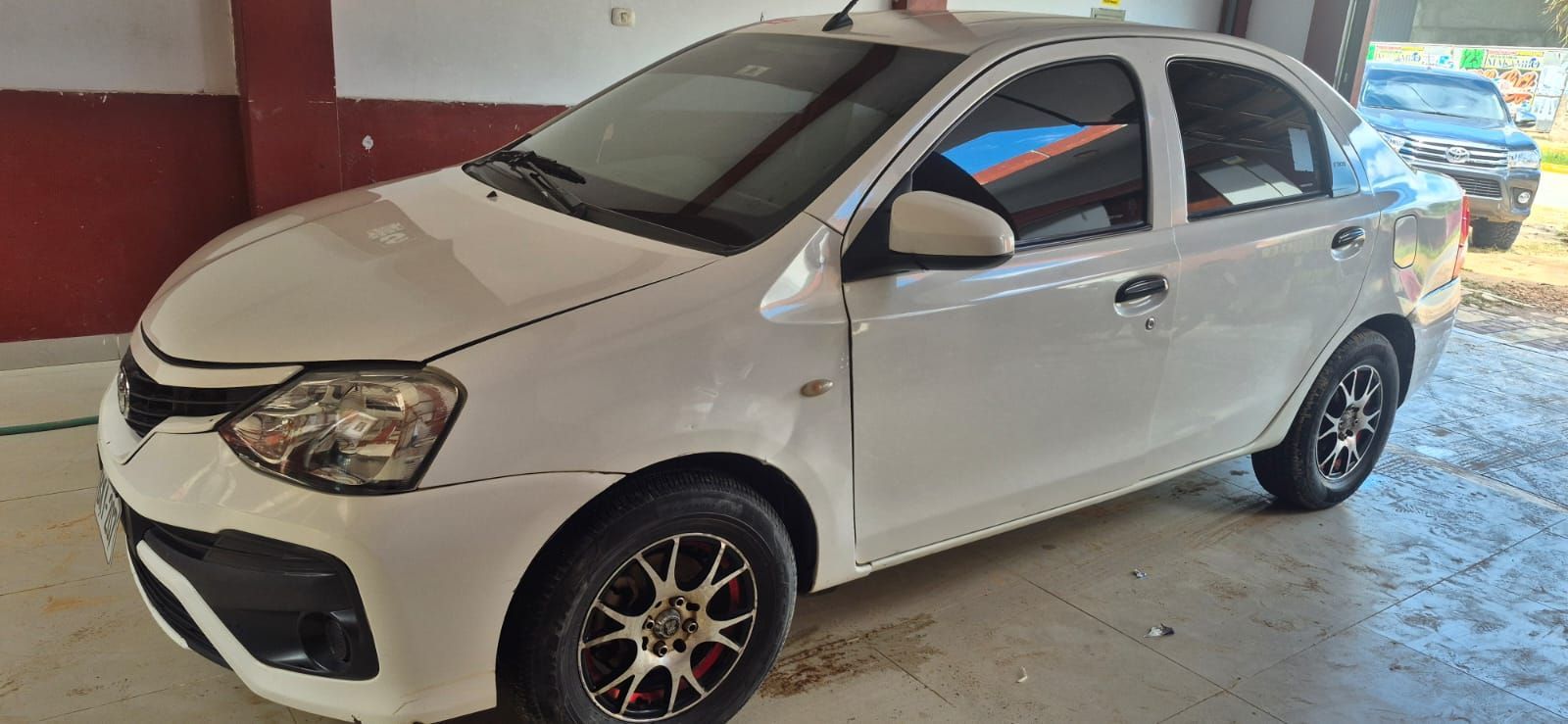 Aparcamiento cubierto con filas de coches aparcados y una furgoneta blanca bajo un gran techo.