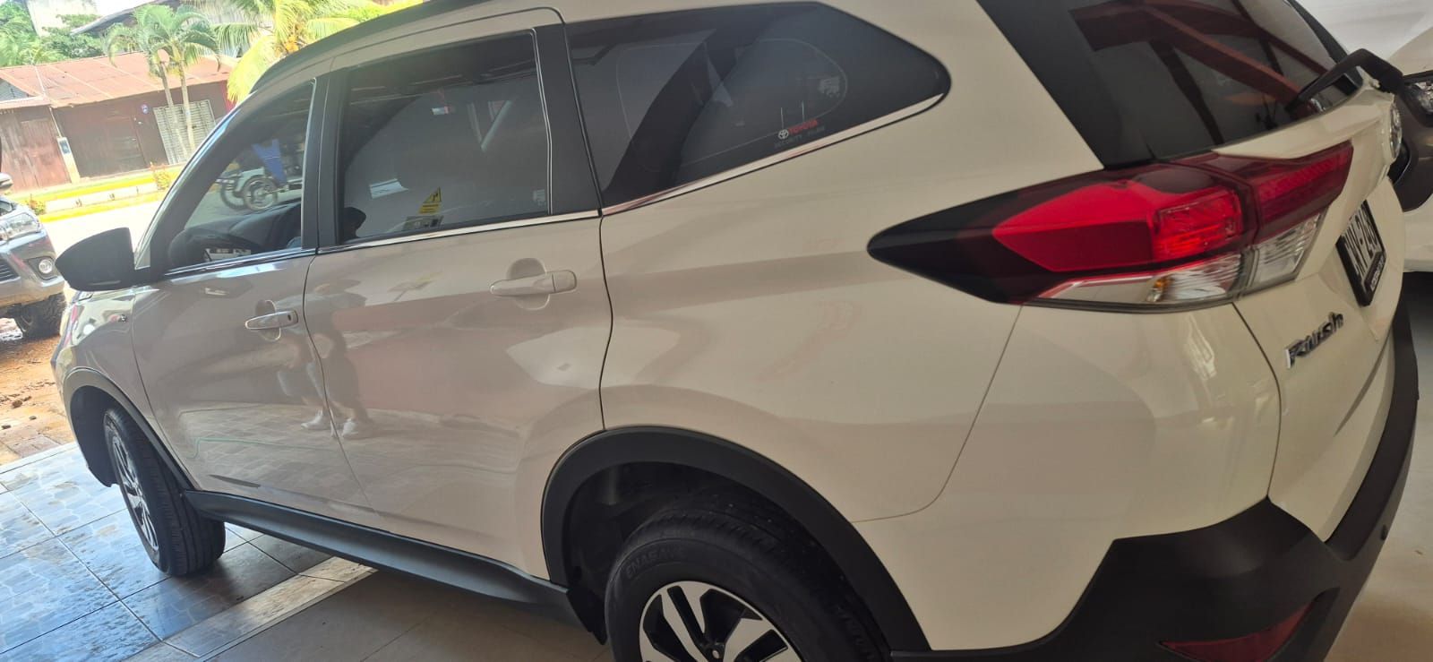 Aparcamiento cubierto con filas de coches aparcados y una furgoneta blanca bajo un gran techo.