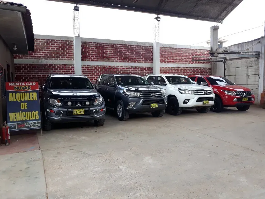 Lote de autos usados ​​con cuatro SUV estacionados bajo un área techada y un letrero de “Quiosco de Veículos”.