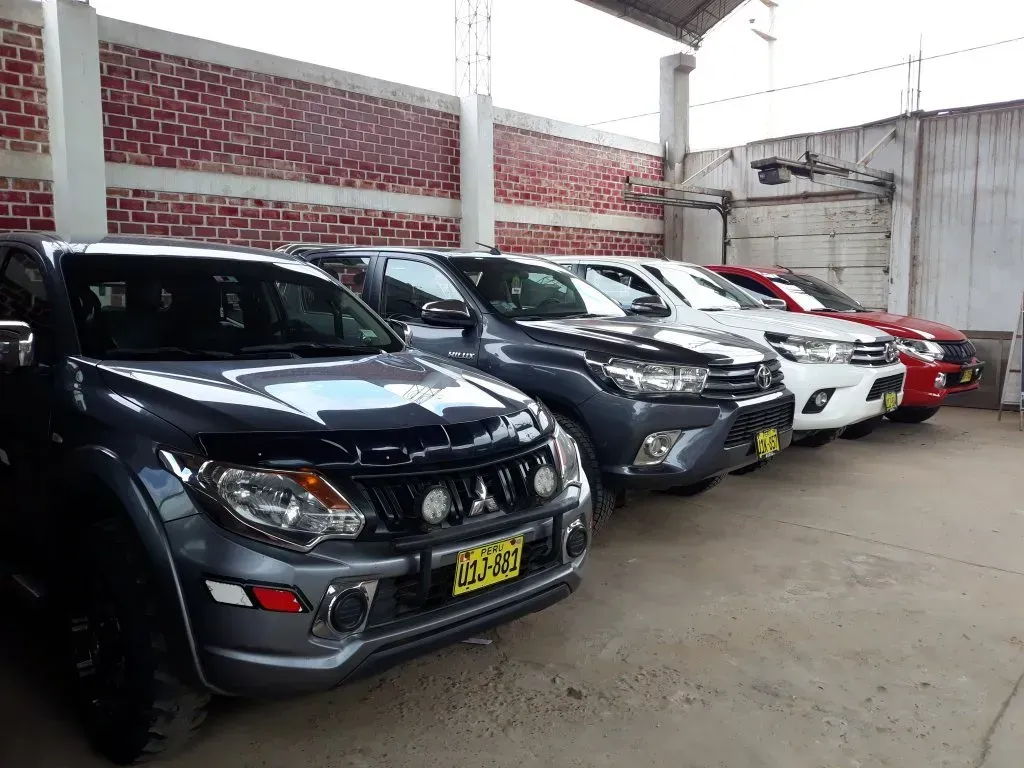 Fila de coches aparcados en un aparcamiento cubierto, entre los que se incluyen vehículos negros, grises, blancos y rojos.