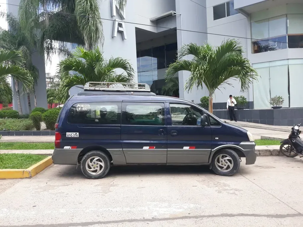 Una furgoneta azul oscuro aparcada junto a un edificio moderno con palmeras y una motocicleta cerca.