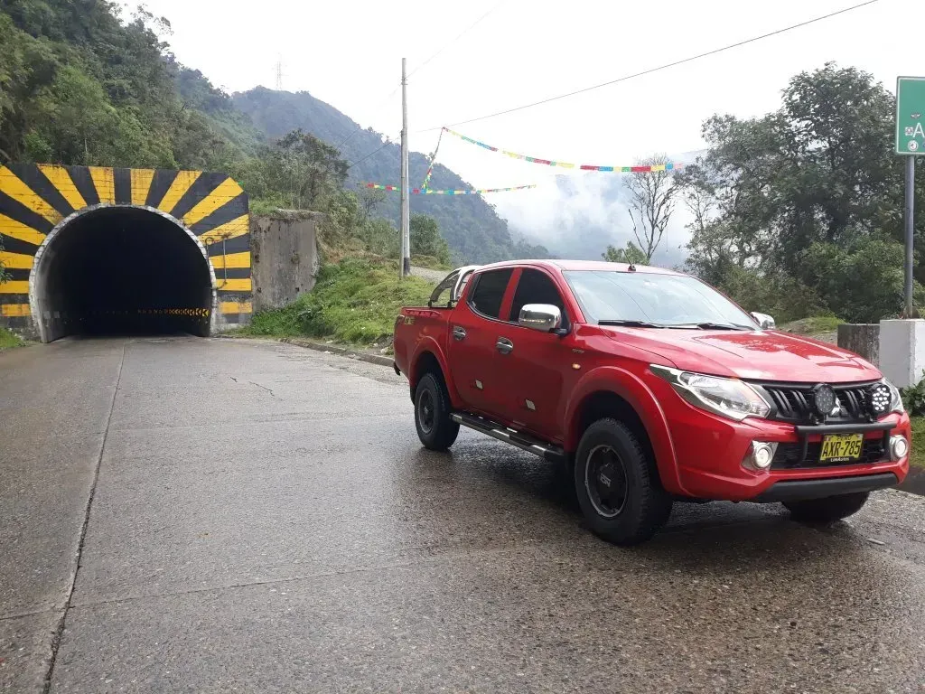 Camioneta roja en una carretera mojada junto a la entrada de un túnel a rayas negras y amarillas en las montañas cubiertas de niebla.