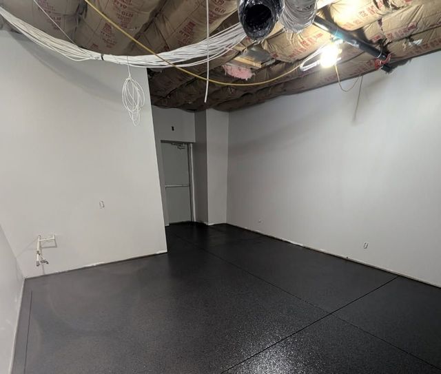 Empty room with black floor, white walls, and exposed ceiling ducts and wiring