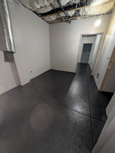 Empty unfinished room with dark floor, gray walls, exposed ceiling insulation, and a doorway in back