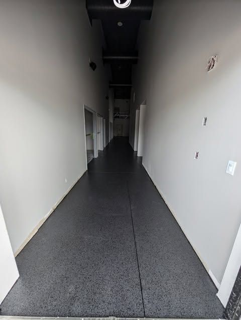 Long, empty gray hallway with white walls and doors, viewed from one end.