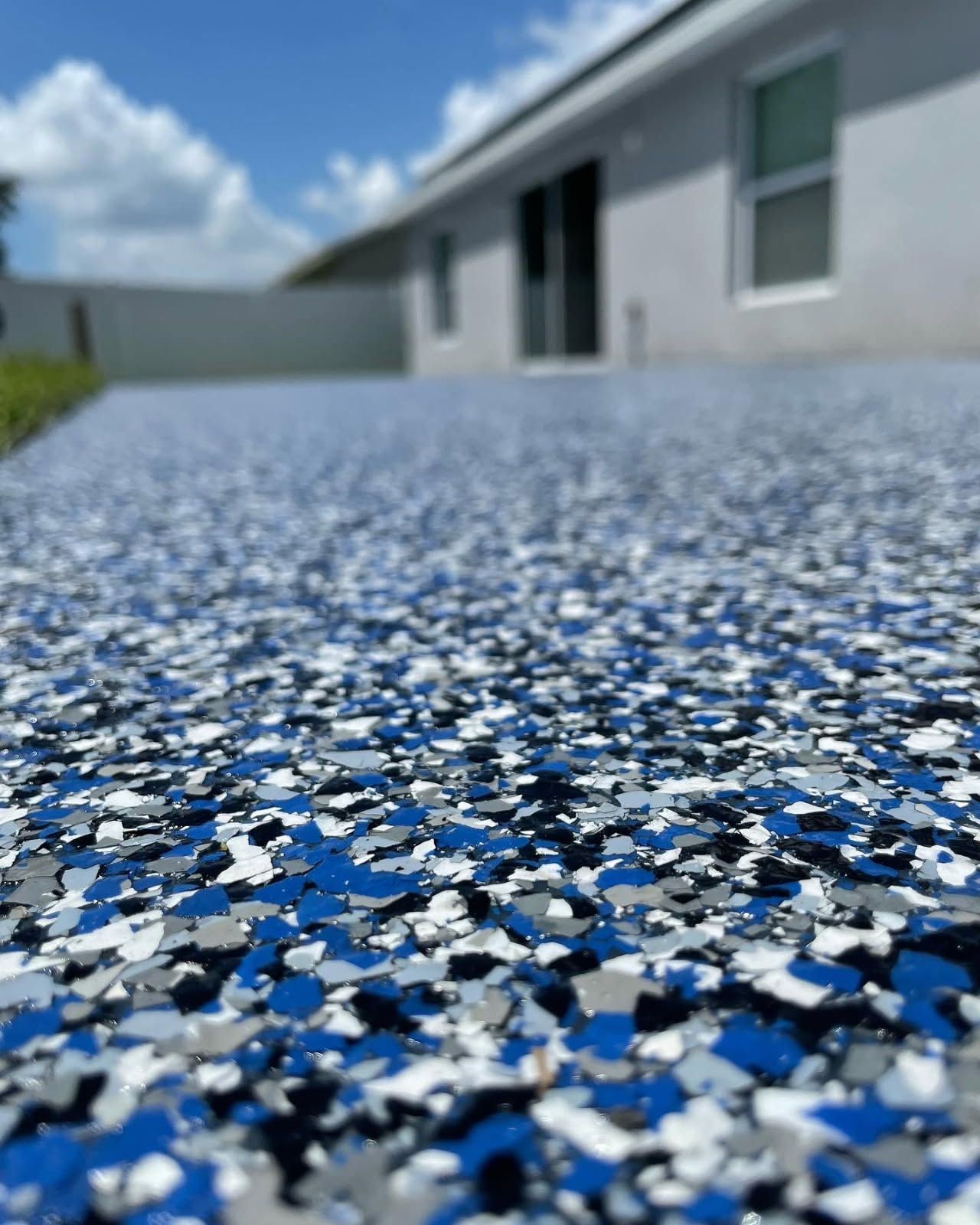 Blue, white, and black speckled textured ground beside a blurred house under a blue sky
