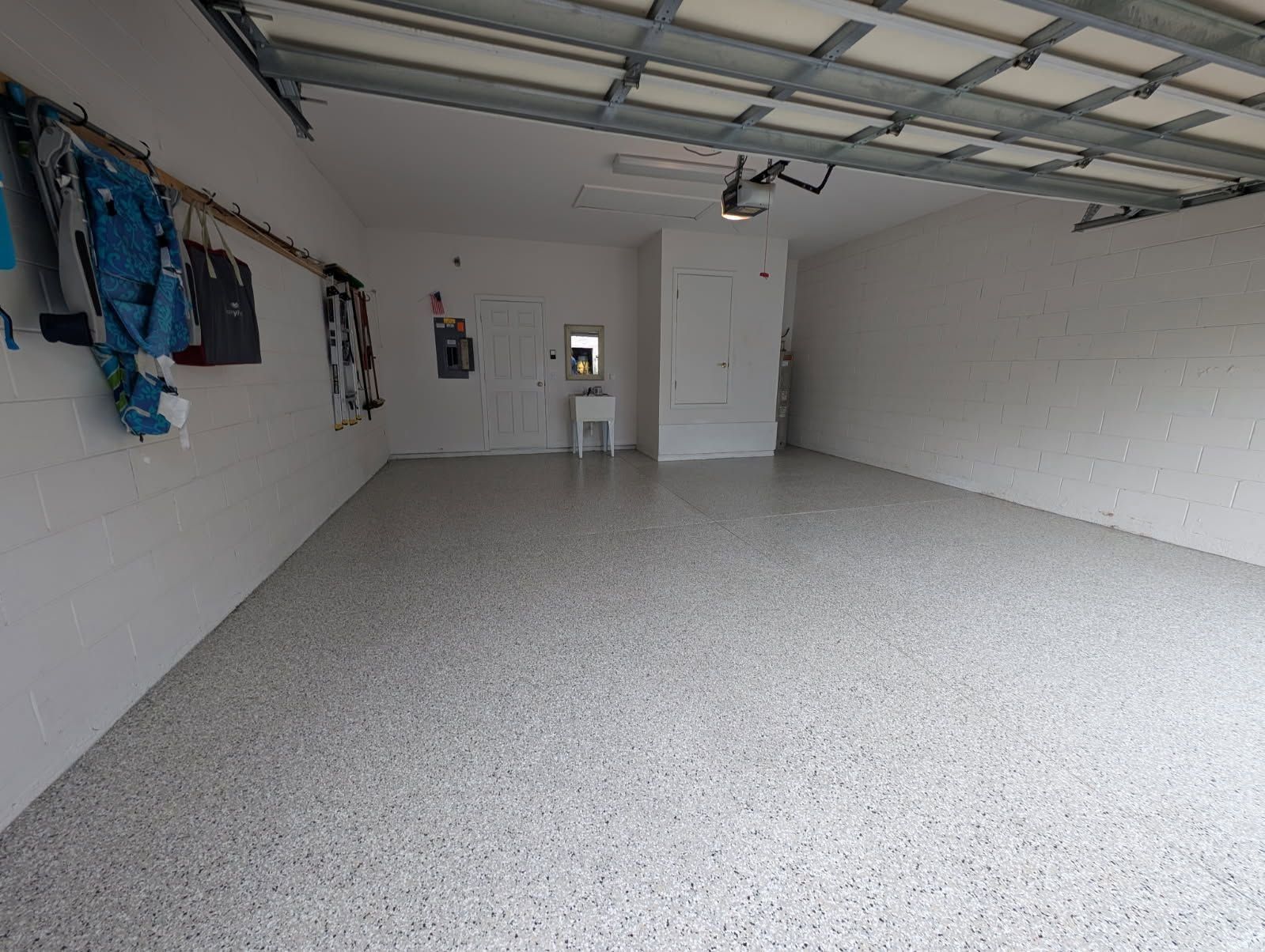 Empty white garage with speckled floor, hanging clothes on the left wall, and a chair near the back door