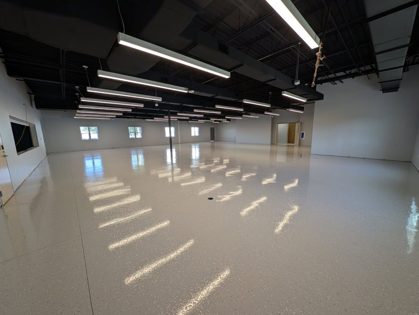 Empty polished industrial room with white speckled floor, black ceiling beams, and bright overhead lights