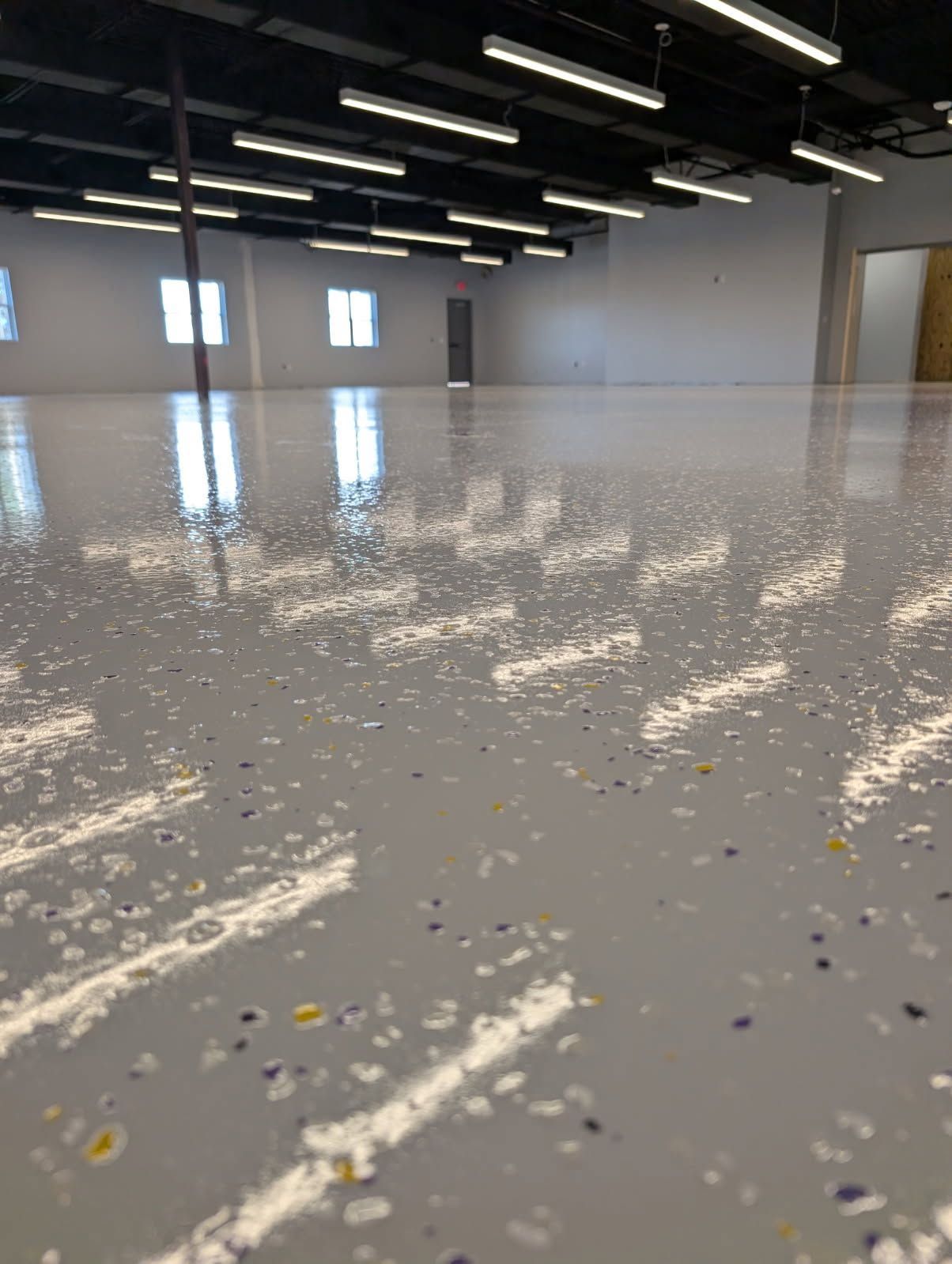 Empty indoor warehouse with a glossy white floor reflecting overhead lights and windows
