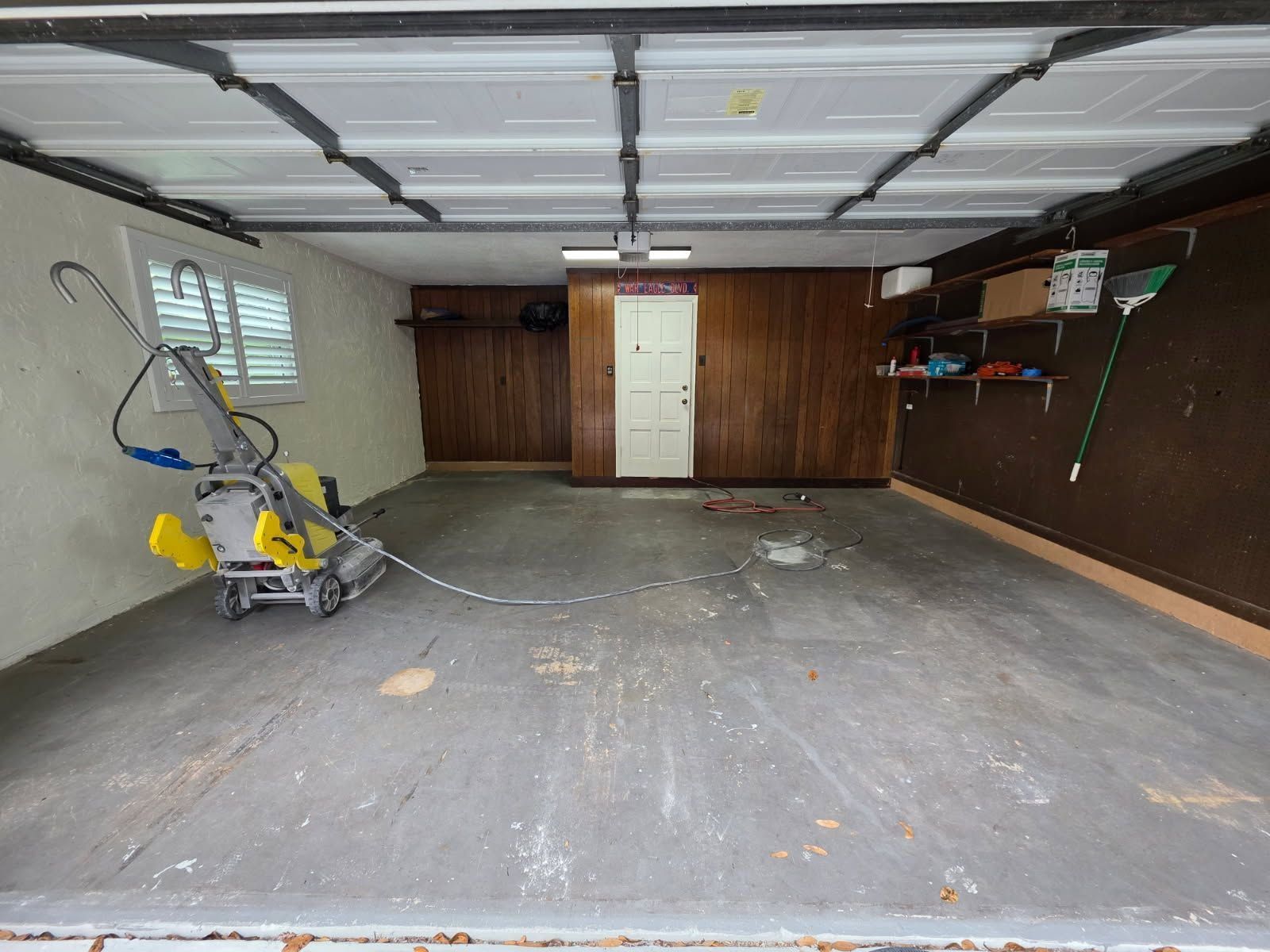 Empty garage interior with concrete floor, overhead door opener, shelves, and a yellow miter saw on the left
