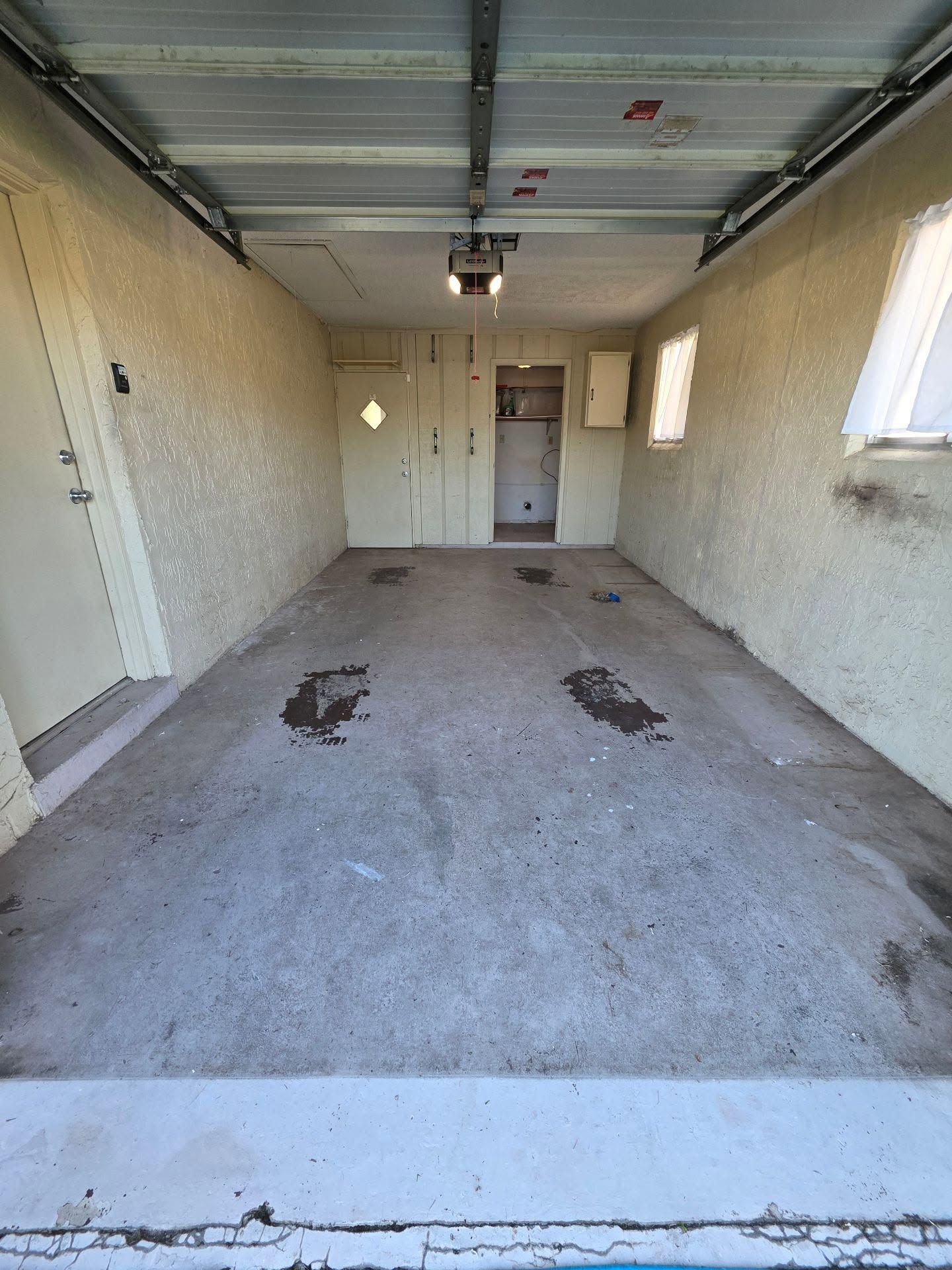 Empty garage with concrete floor, white walls, and windows, viewed from the open door