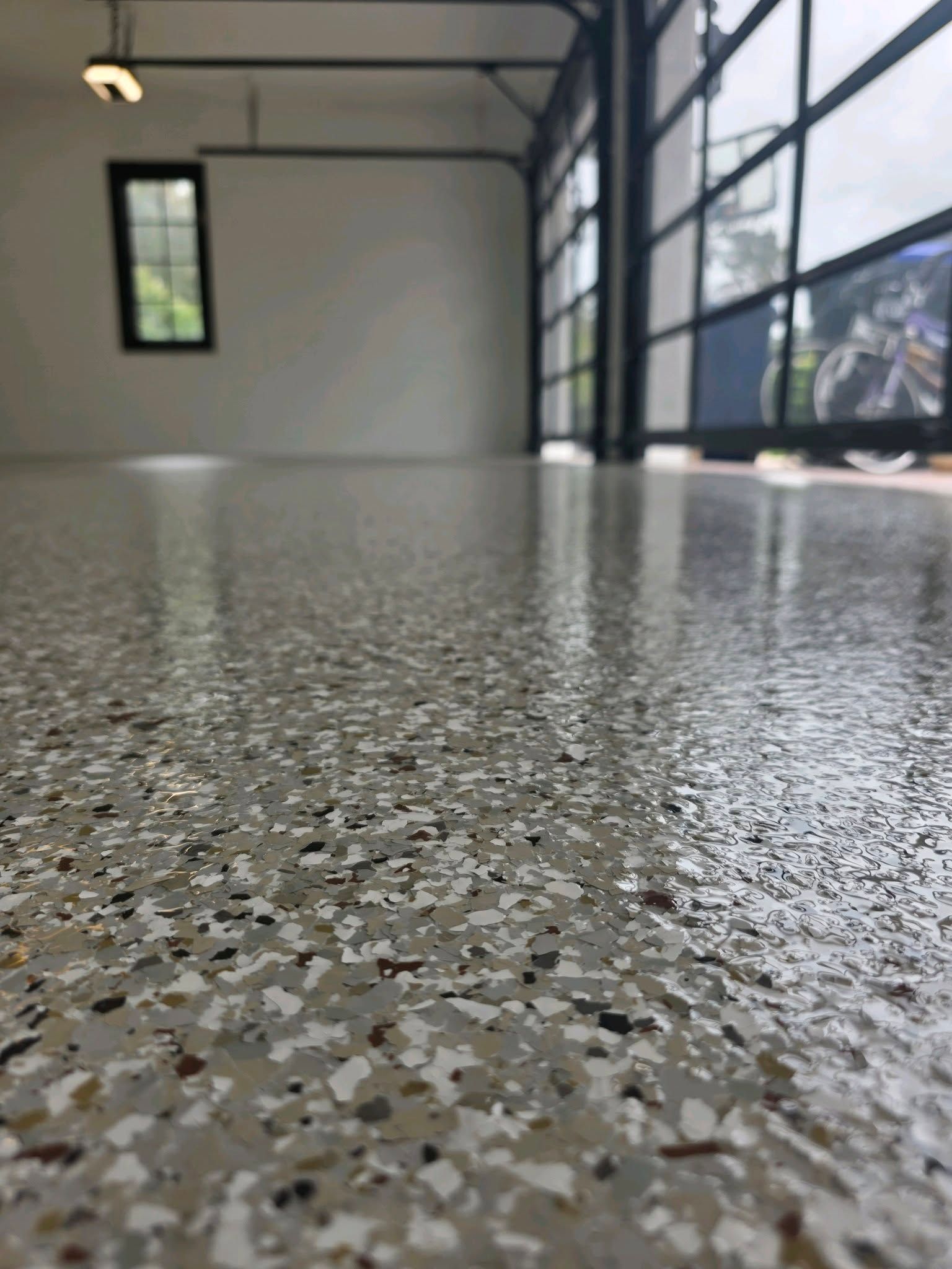 Empty garage with speckled epoxy floor and large open door letting in daylight