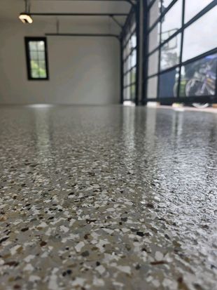 Empty garage with speckled epoxy floor, window on the left, and open glass door to the outside.