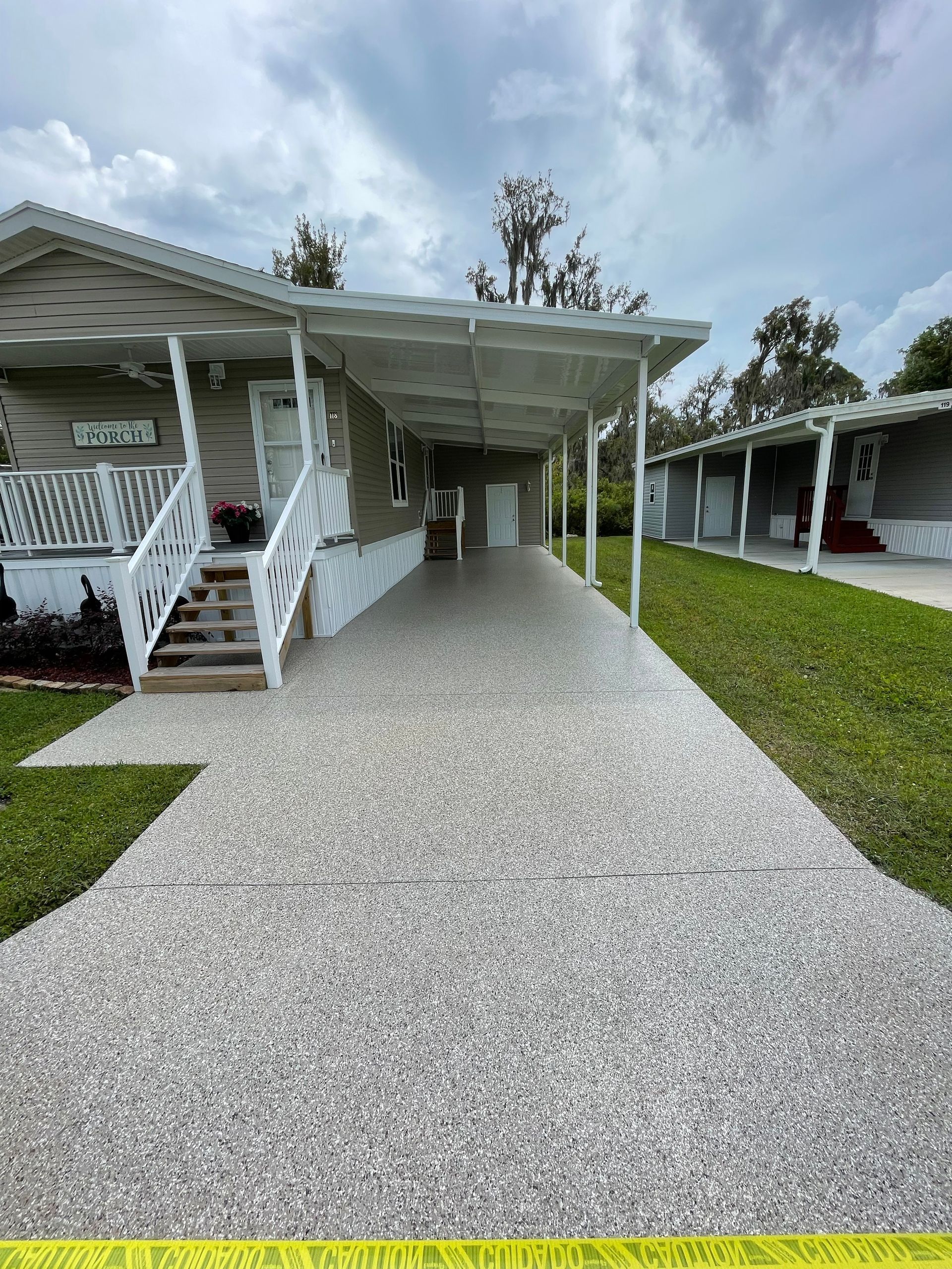 Gravel driveway leading to white mobile homes with covered porches and stairs in a grassy park.