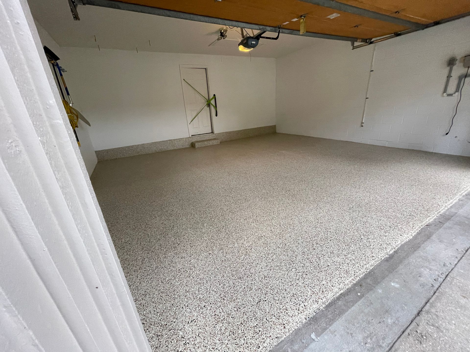 Empty garage with speckled floor, white walls, and an open overhead door partially visible on the left.