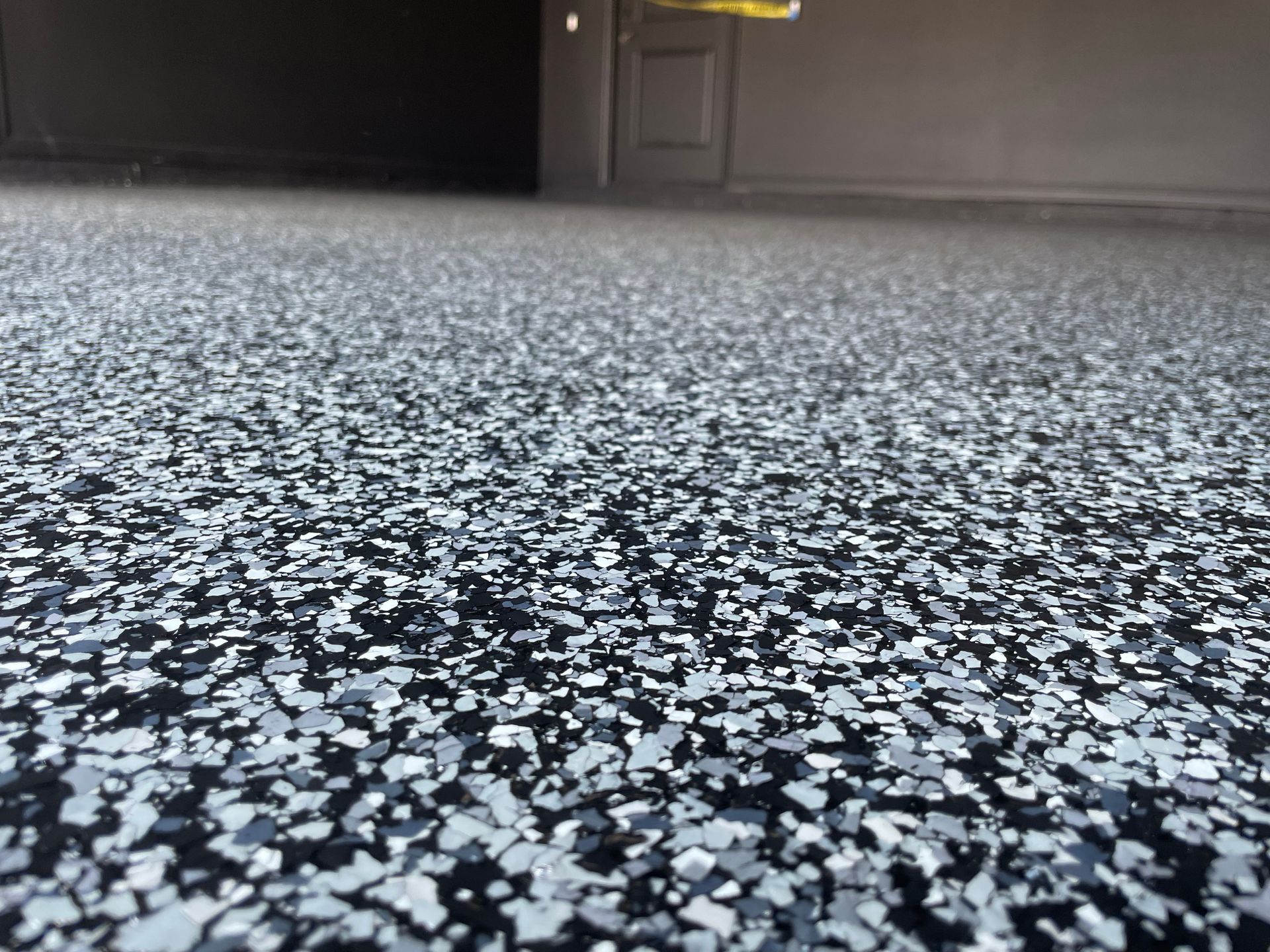Low-angle view of a black speckled floor in a dim indoor room with a door in the background
