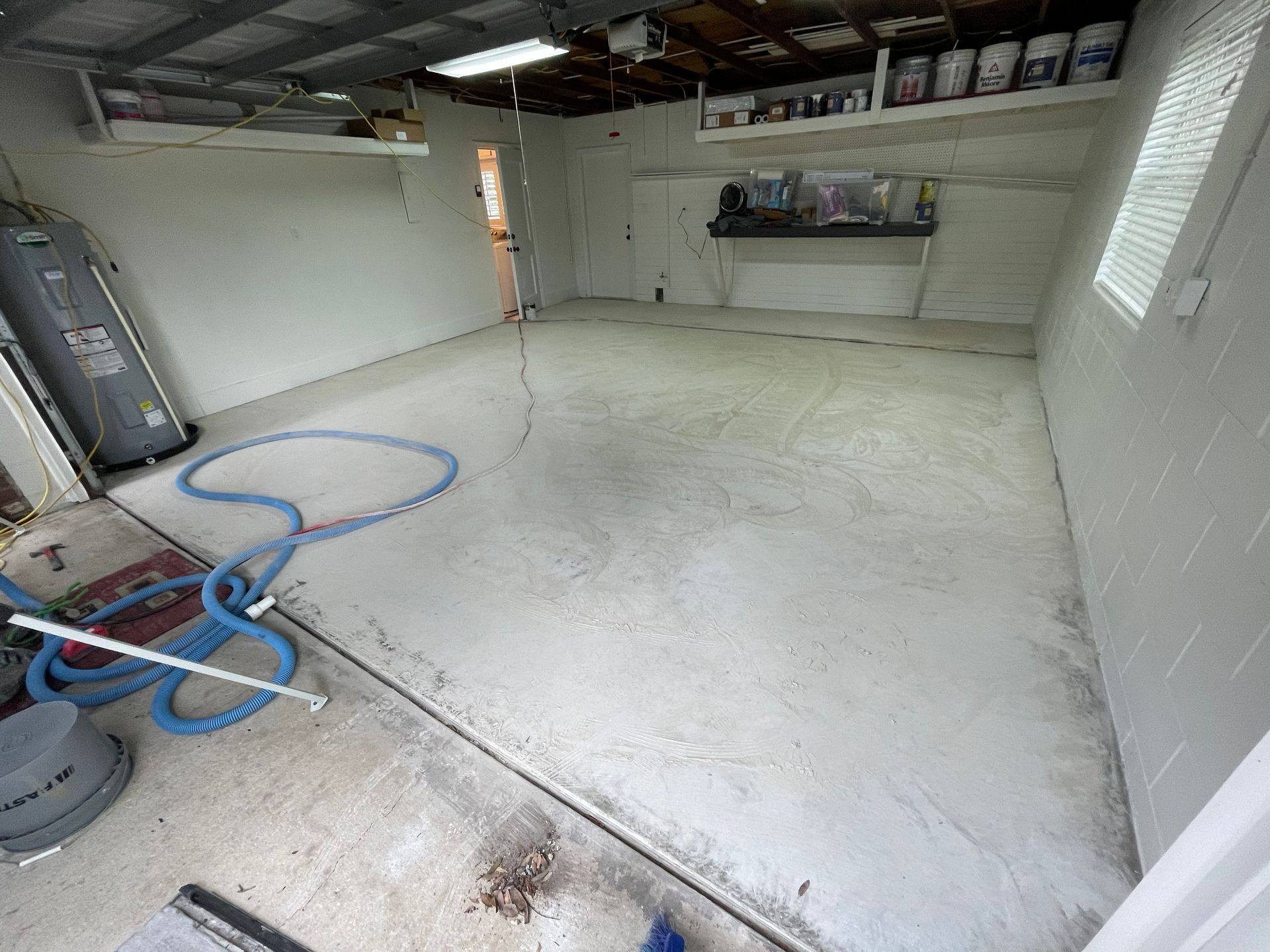 Empty garage with white floor, blue hose on the ground, and shelves along the walls