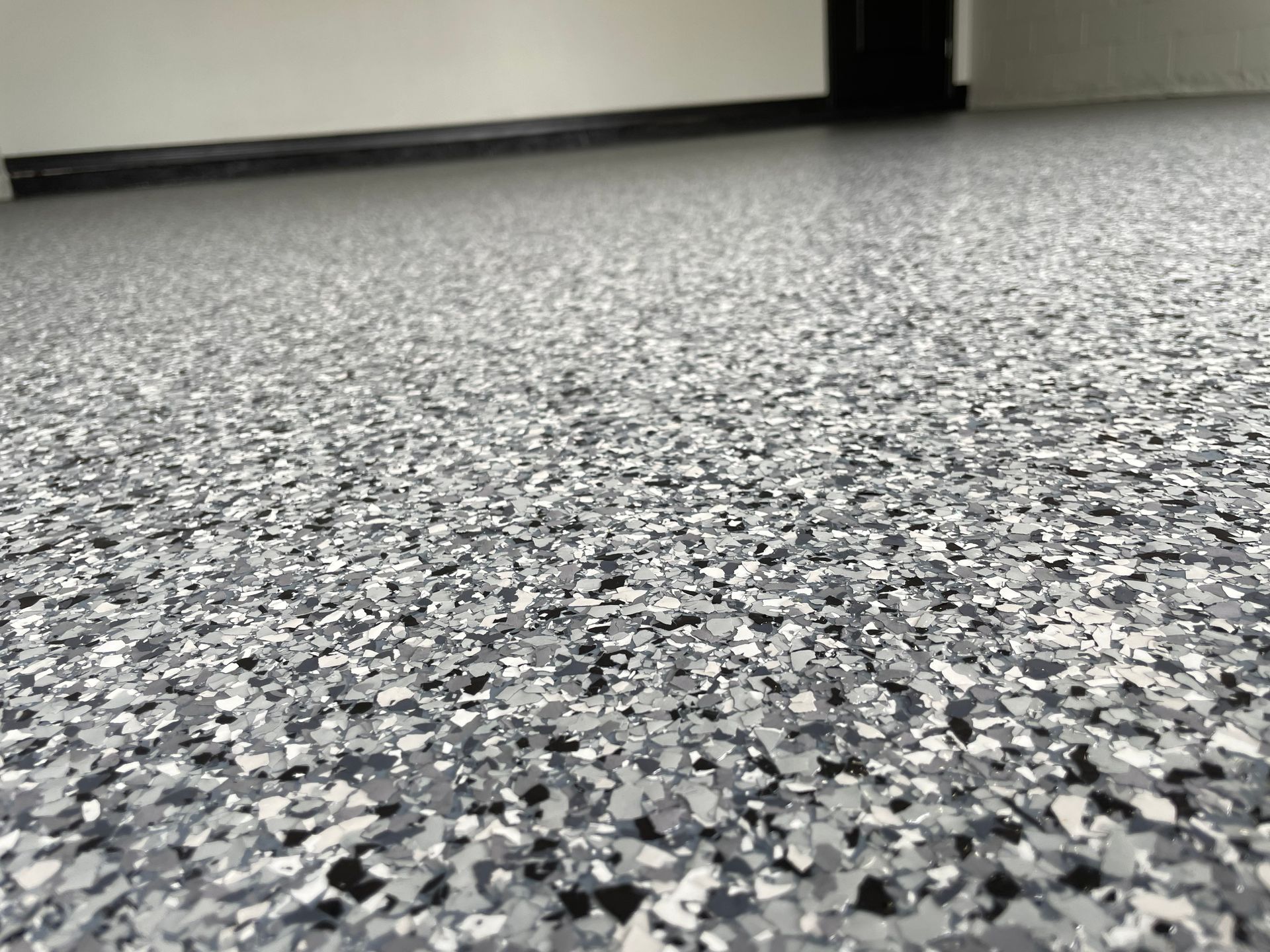 Speckled gray floor with a white wall and black baseboard in the background