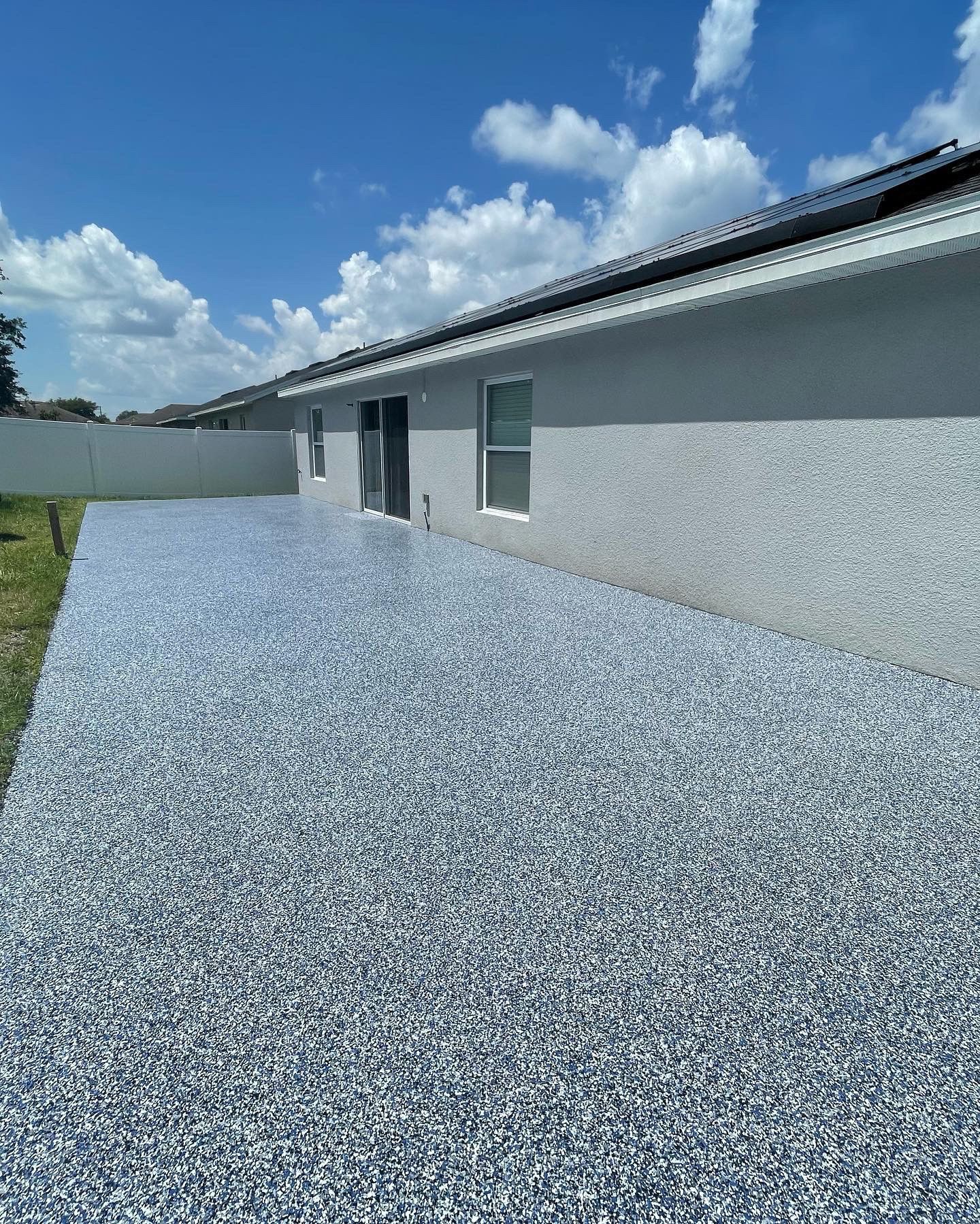 Blue gravel yard beside a gray house under a bright blue sky with clouds