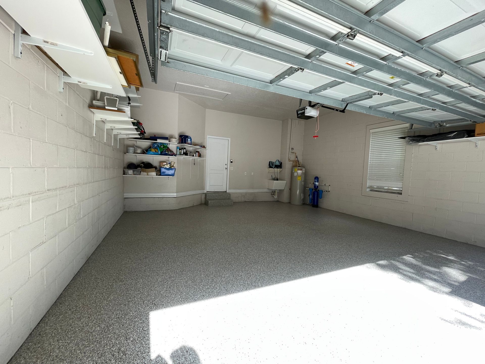 Empty garage interior with white walls, open door, and sunlight on the concrete floor