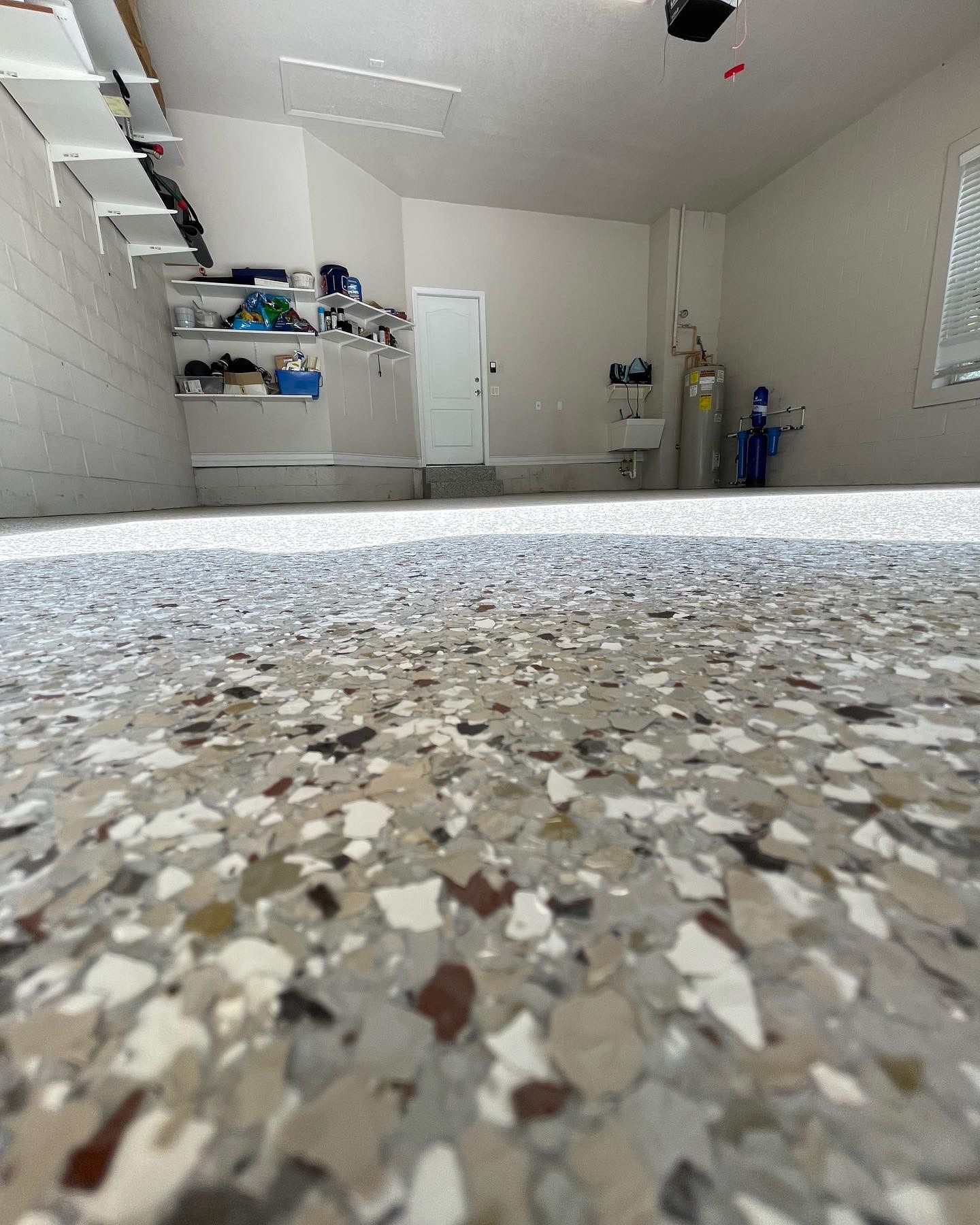 Garage interior with speckled epoxy floor, white walls, shelves, and a closed door.