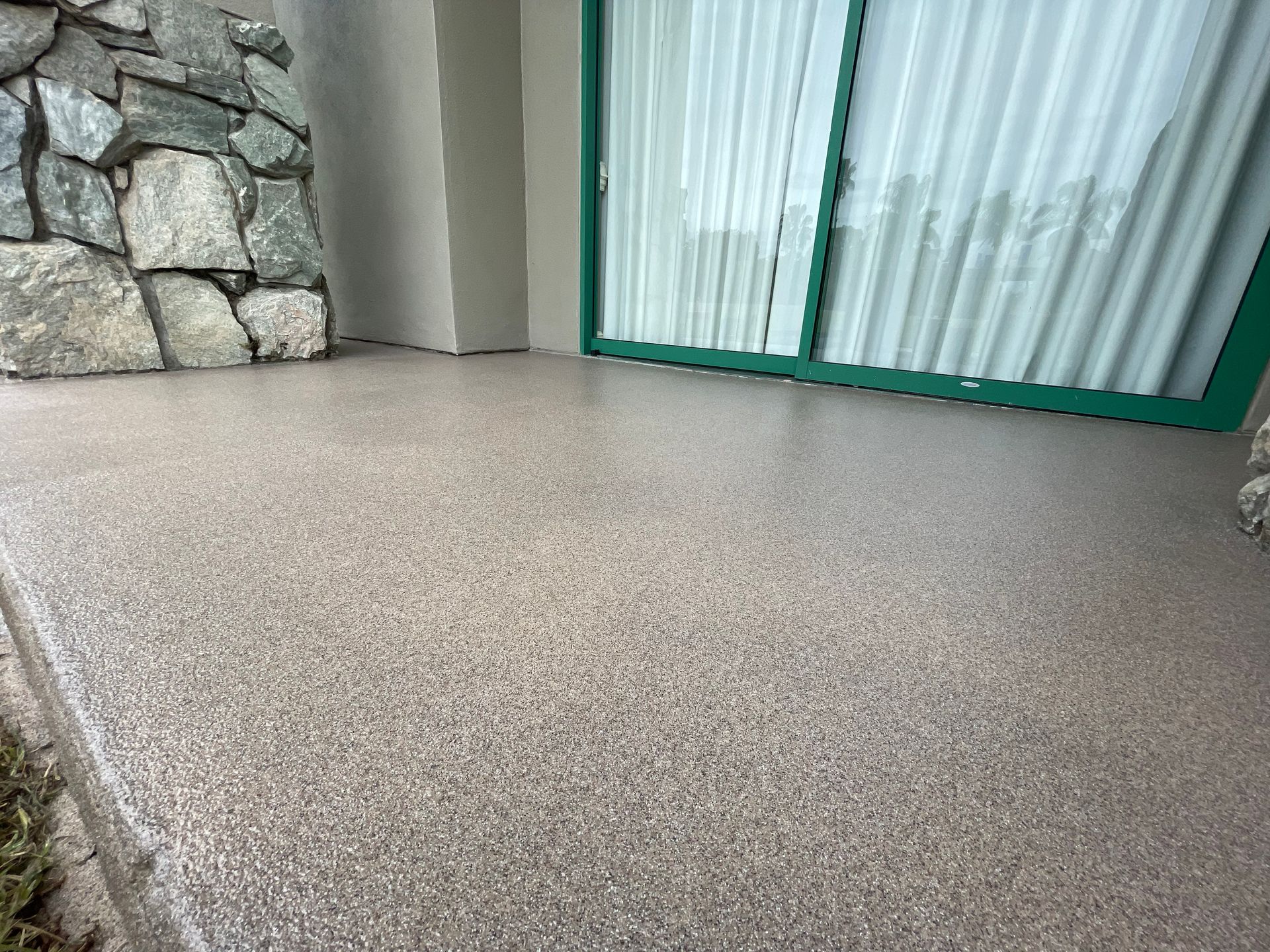 Textured patio floor beside a stone wall and sliding glass door with green trim