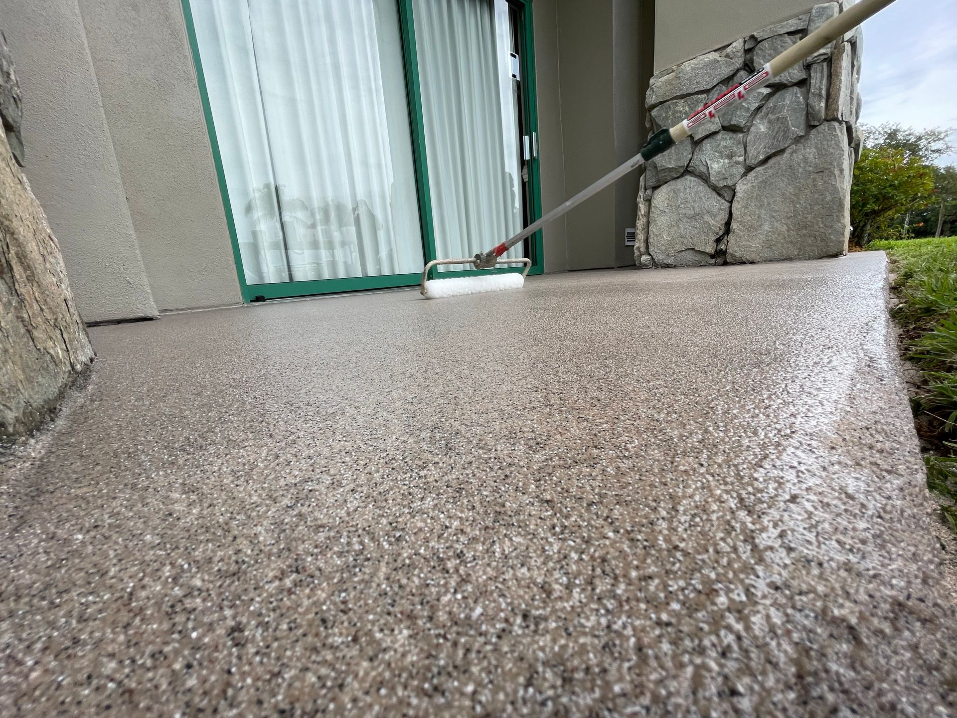 Textured concrete ramp leading to a doorway, with a stone wall and metal railings.
