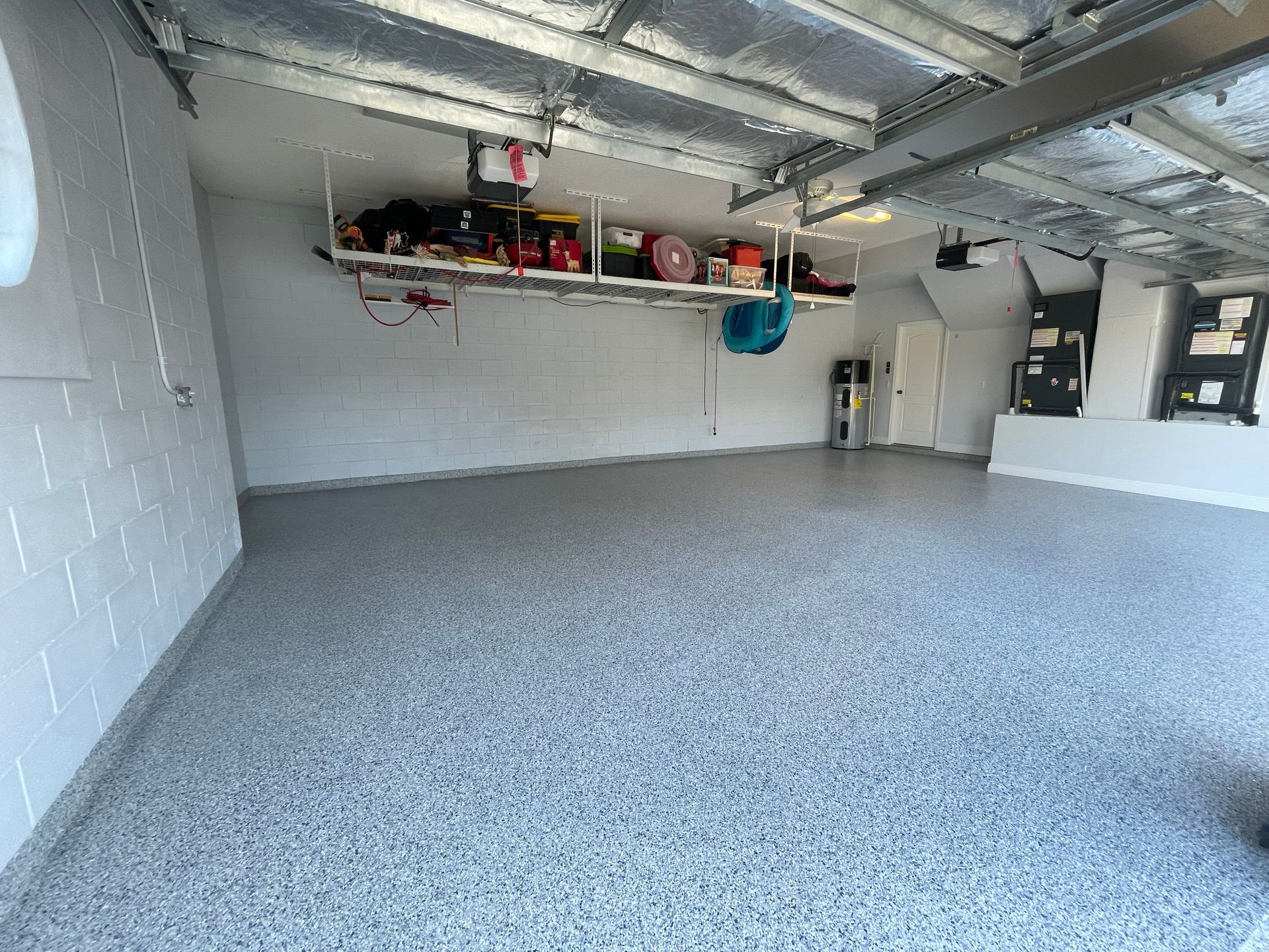 Empty garage with gray speckled floor, white walls, overhead storage shelves, and visible ceiling ductwork