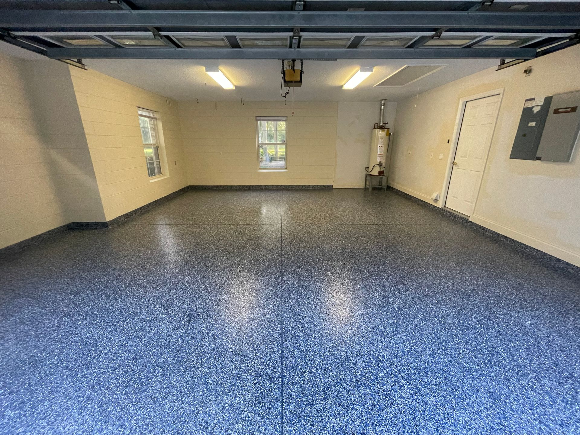 Empty garage with blue speckled floor, beige walls, and windows along the back and side.