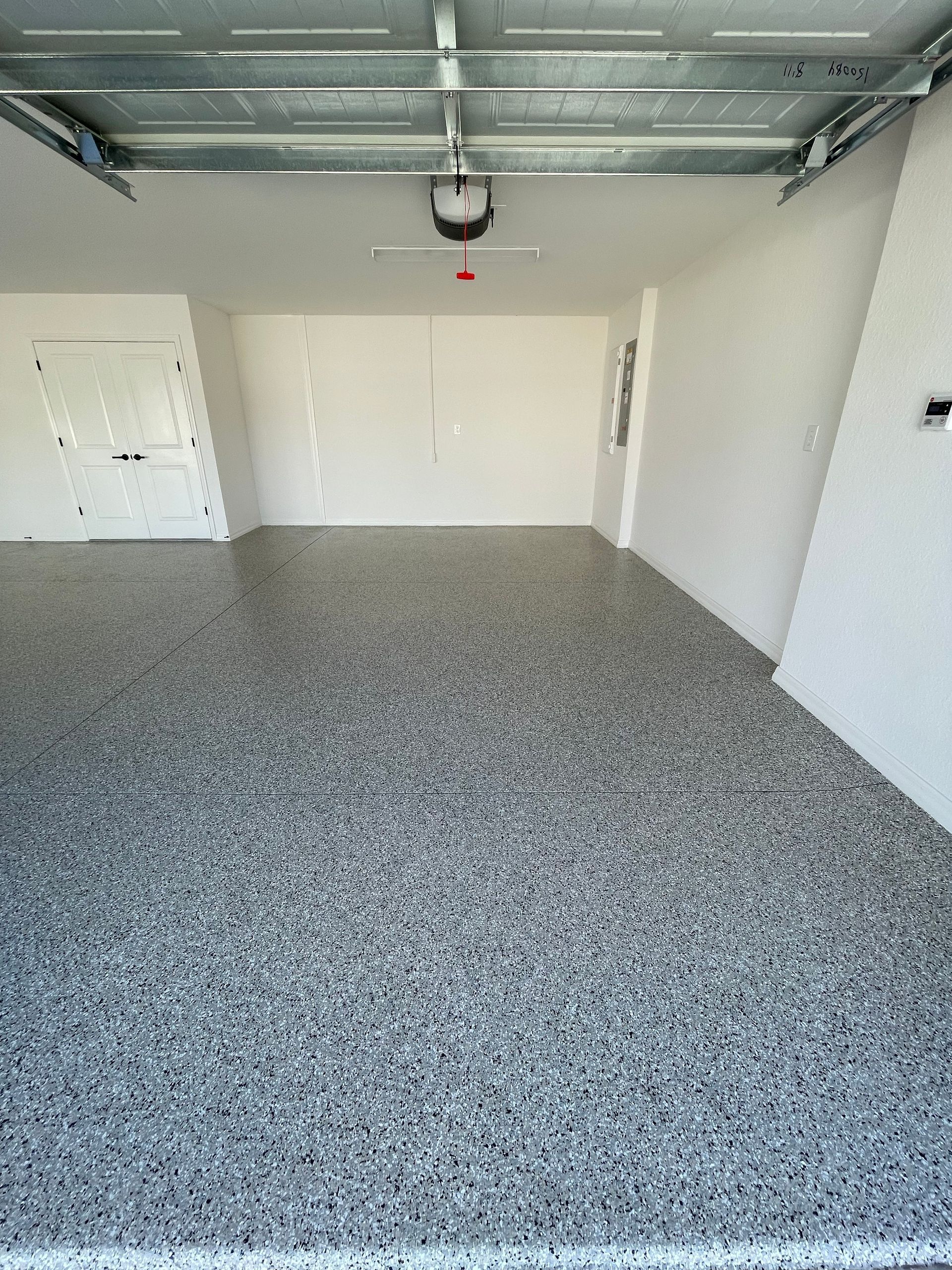 Empty garage with speckled floor, white walls, and an open ceiling-mounted garage door opener.