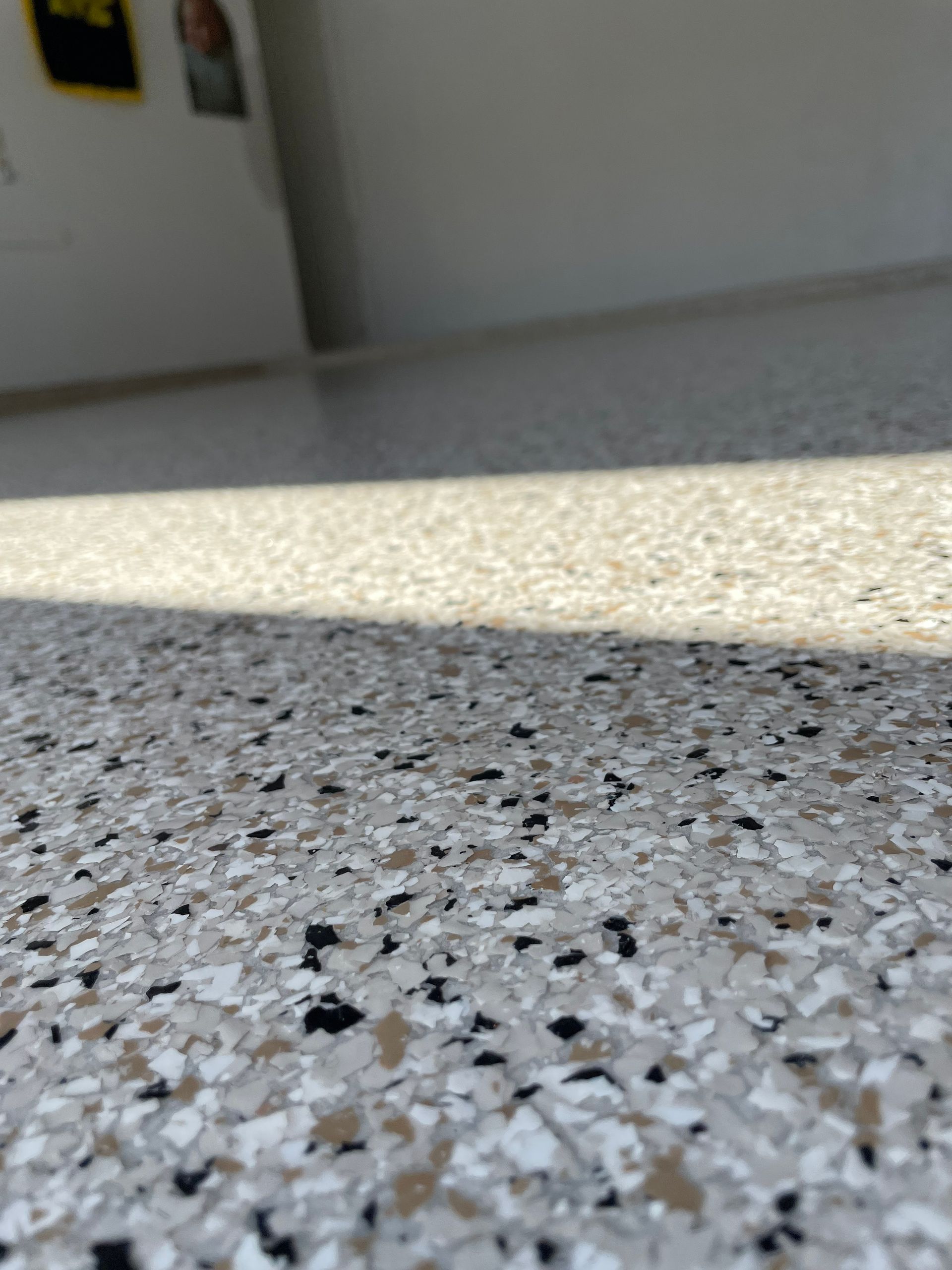 Close-up of a speckled terrazzo floor with sunlight and a shadowed wall in the background
