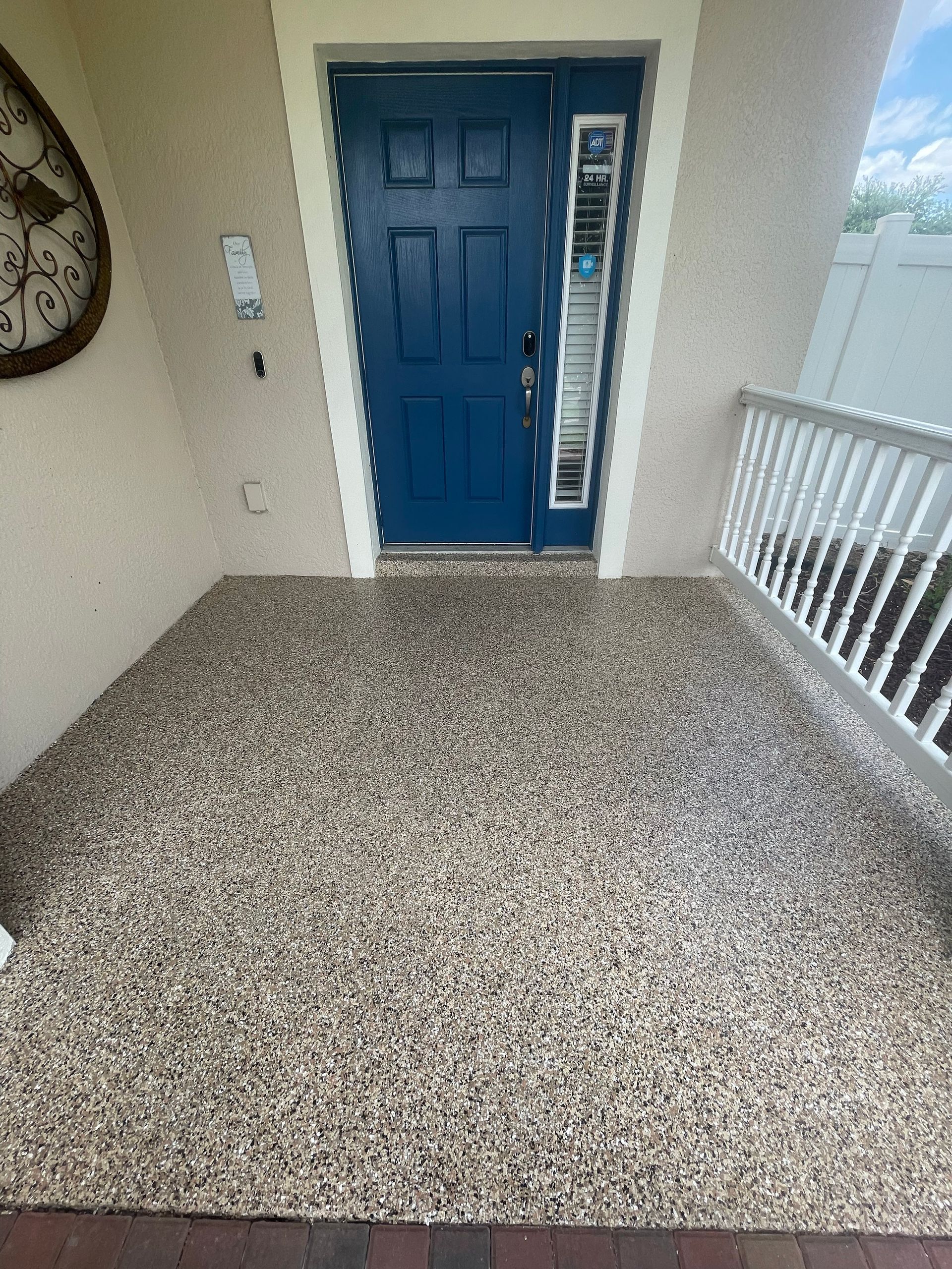 Blue front door beside railing on a covered apartment entryway porch with speckled flooring.
