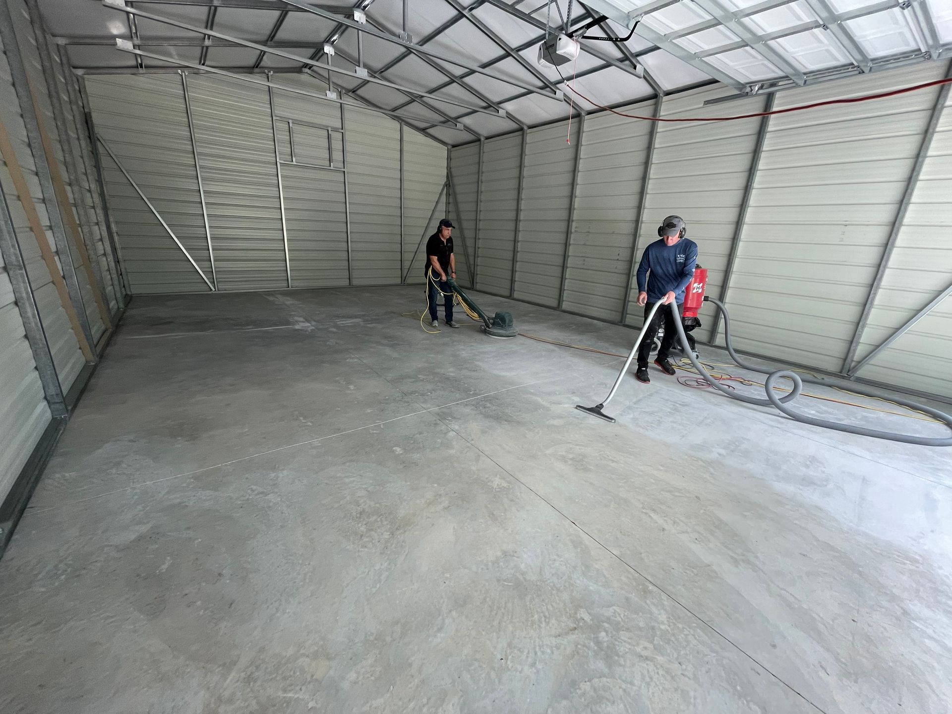 Workers cleaning a large empty metal garage with a pressure washer on the concrete floor