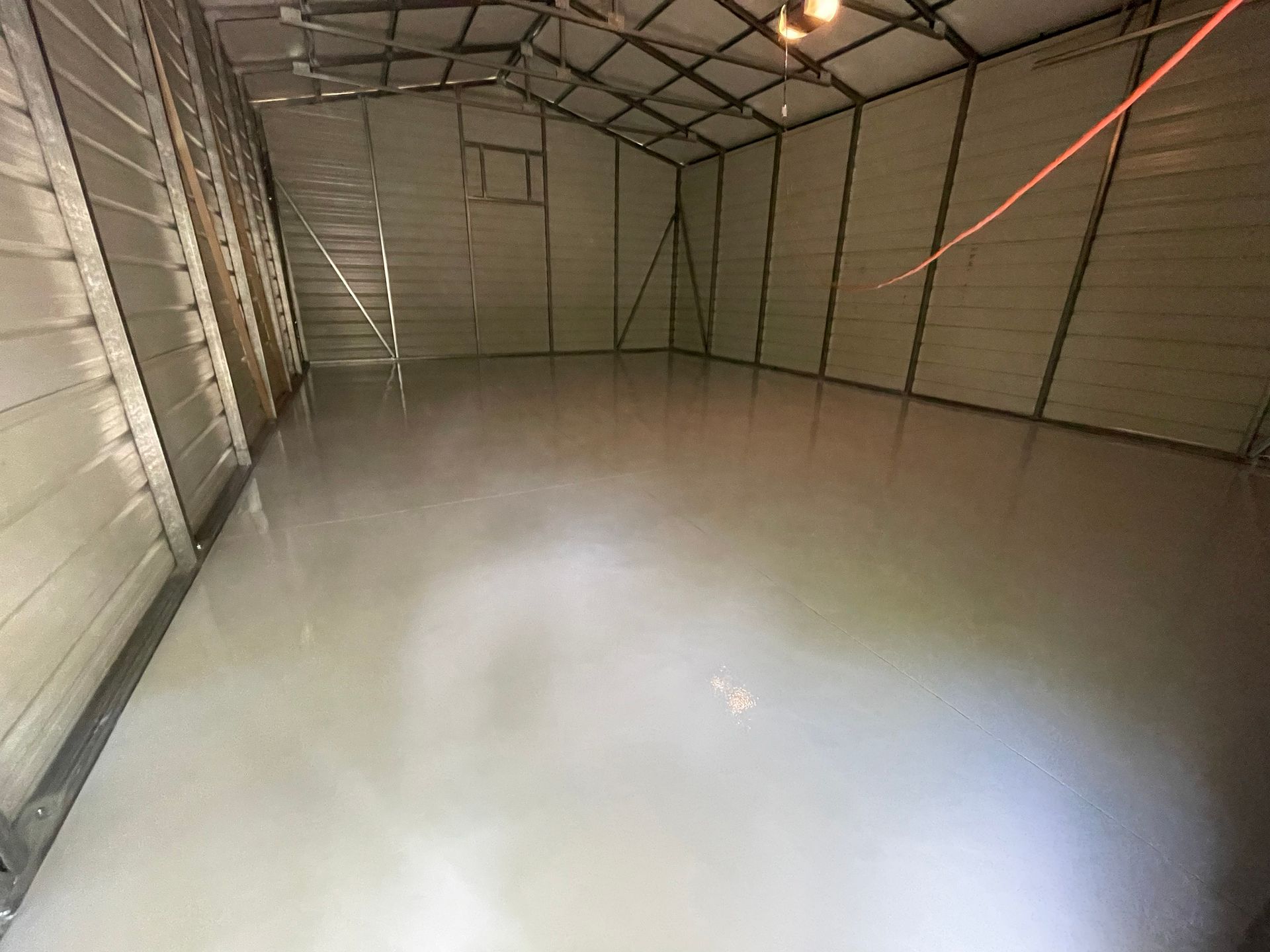 Empty garage with a newly poured concrete floor and overhead lights.