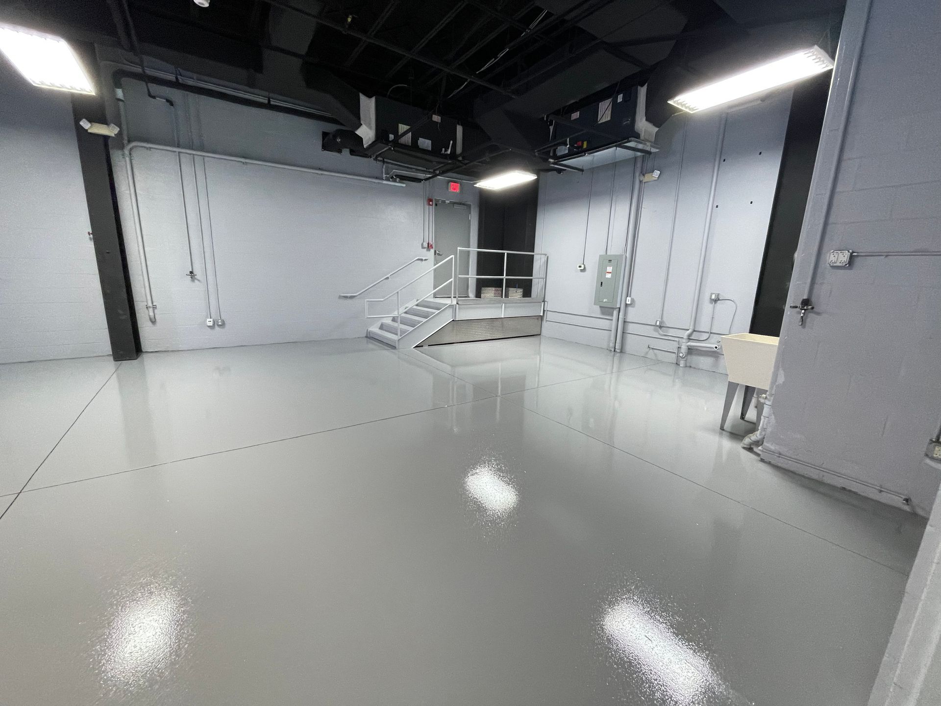 Empty glossy studio room with gray walls, white floor, stairs, and overhead lights