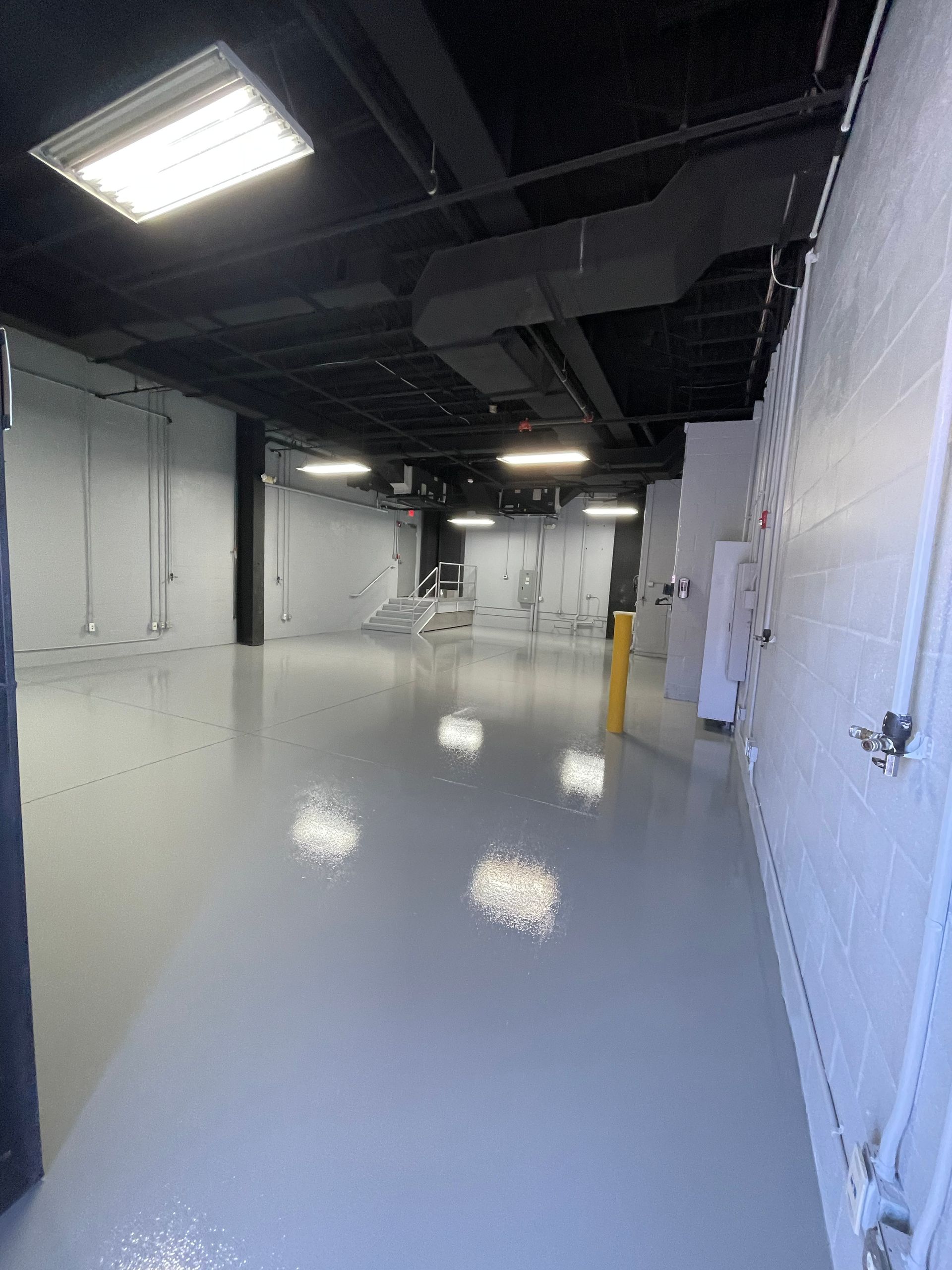 Empty industrial room with white walls, glossy gray floor, and overhead fluorescent lights