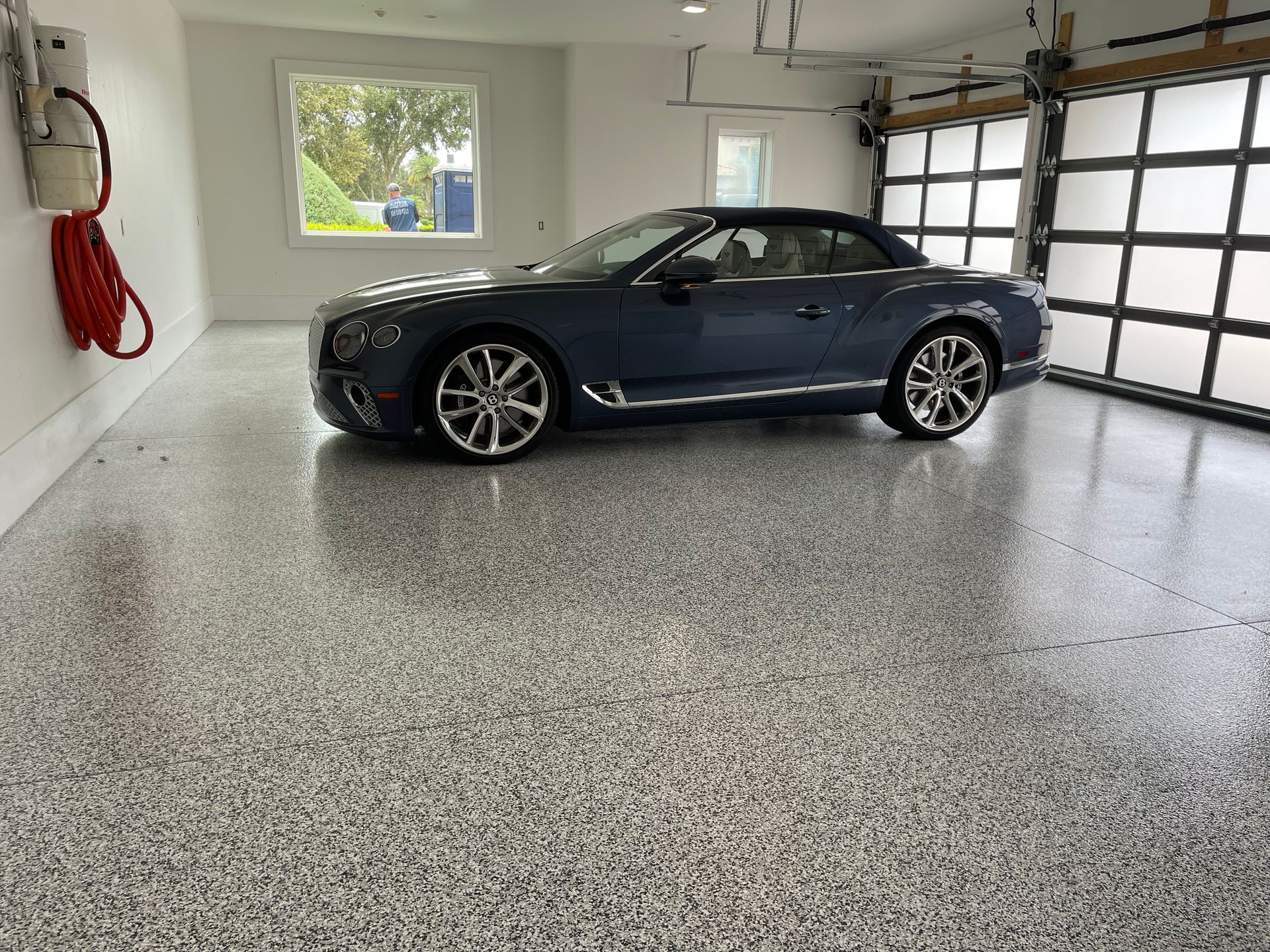 Dark blue convertible parked in a clean garage with speckled epoxy floor and a window.