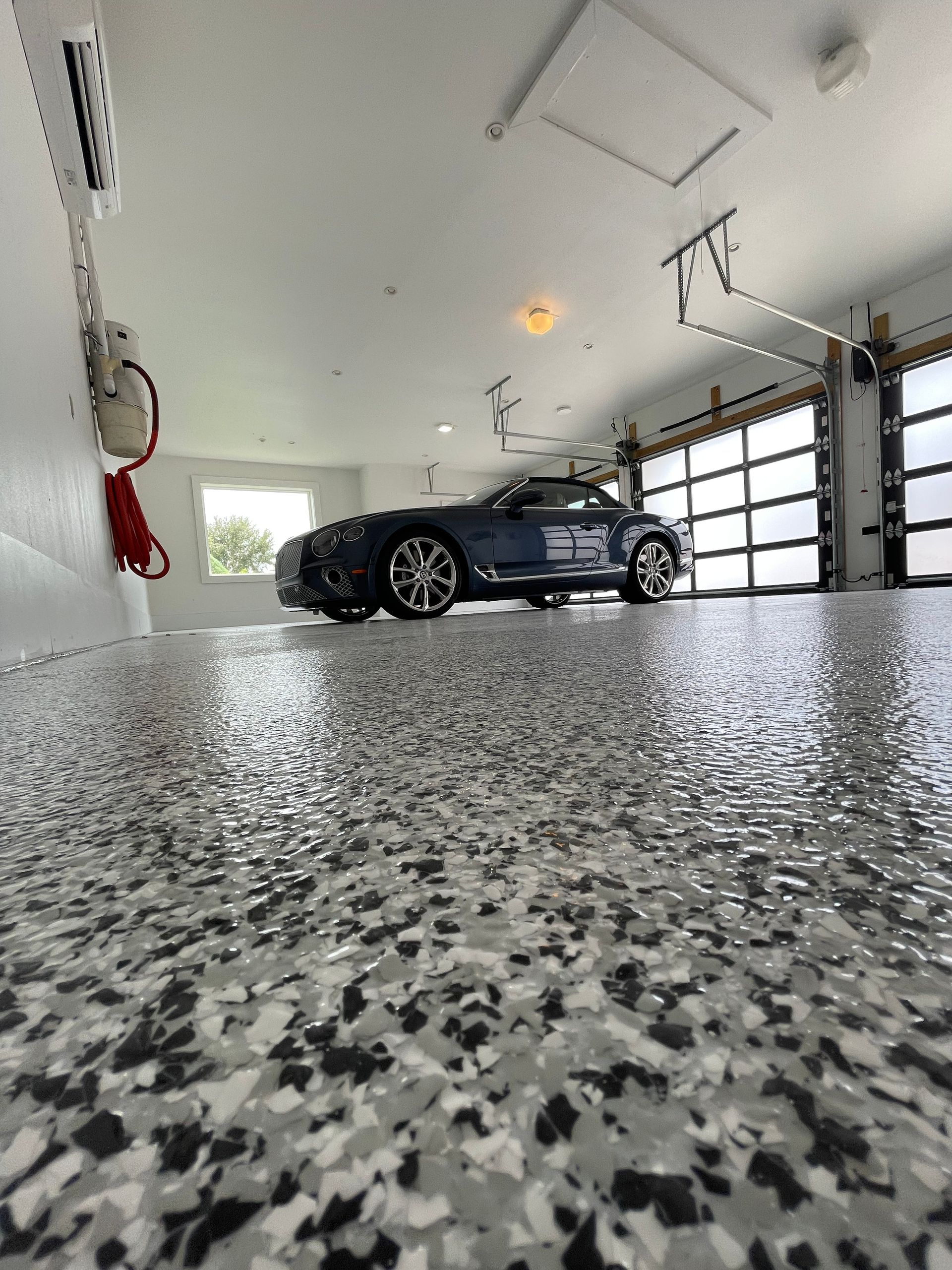 Dark sports car parked in a bright garage with a speckled epoxy floor.