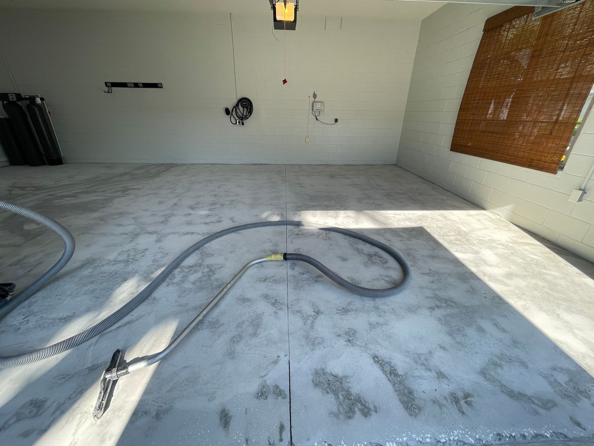Empty garage with white walls, concrete floor, and a hose or cable lying across the floor.