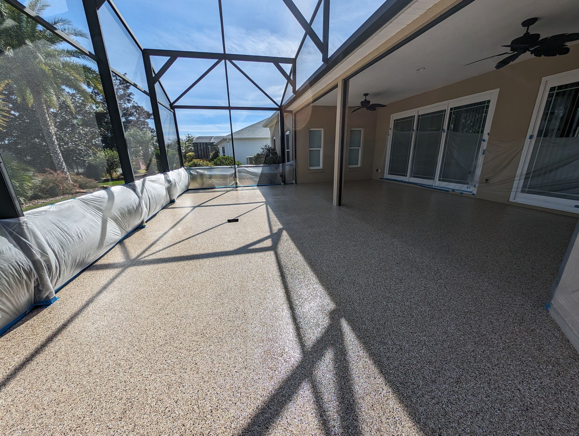 Covered backyard patio with gravel floor, screened roof, and house windows in bright sunlight