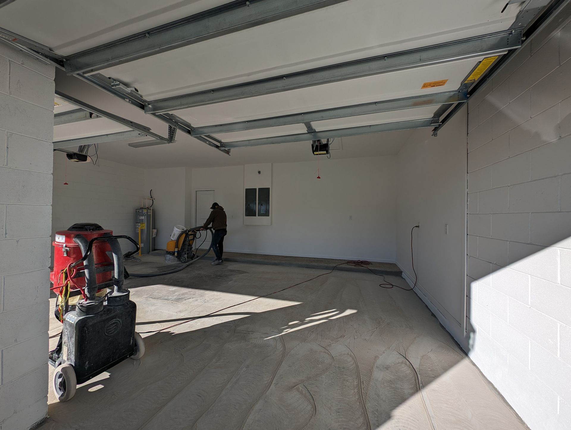 Empty garage with open door, white walls, and construction tools along the left side.