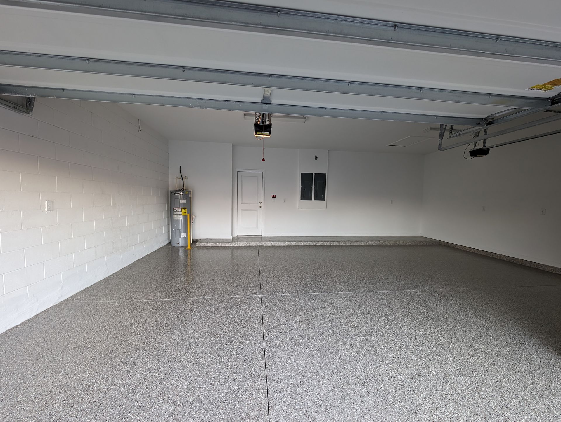 Empty two-car garage with speckled epoxy floor, white walls, and a garage door opener overhead